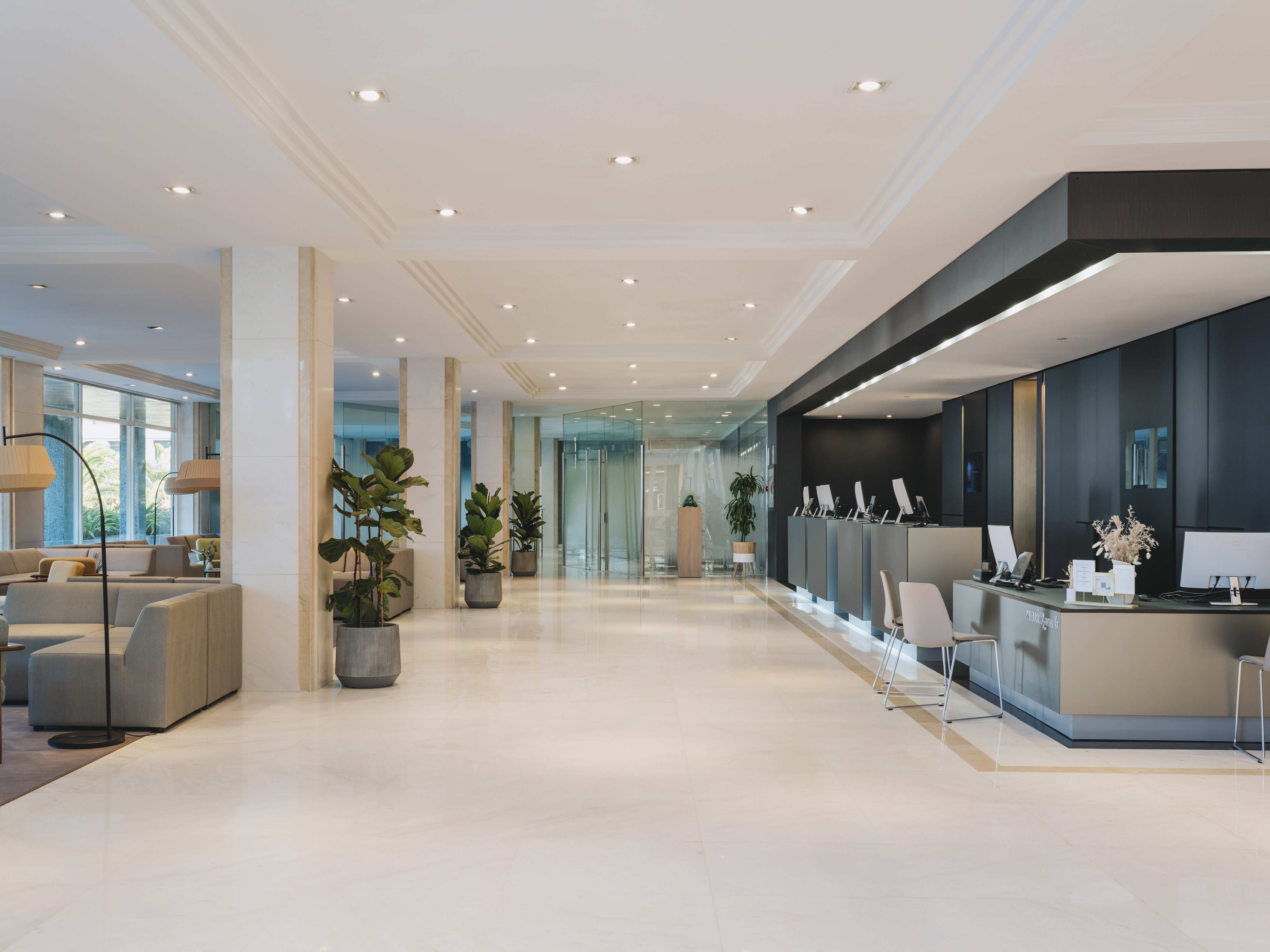 Contemporary hotel lobby with reception desks, lounge area, marble floor, and plants.