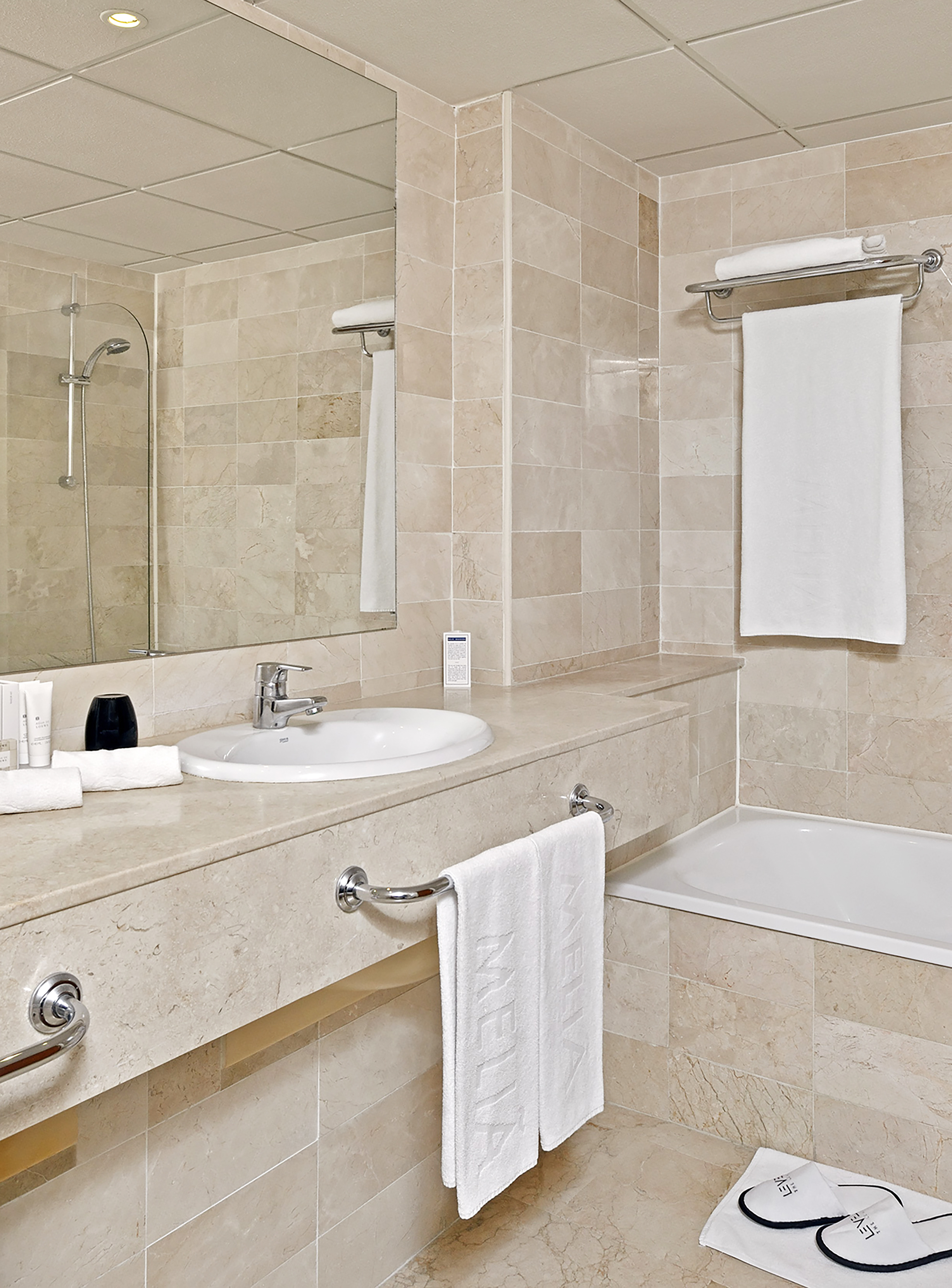 Modern marble bathroom with sink, shower, bathtub, mirror, and white towels.