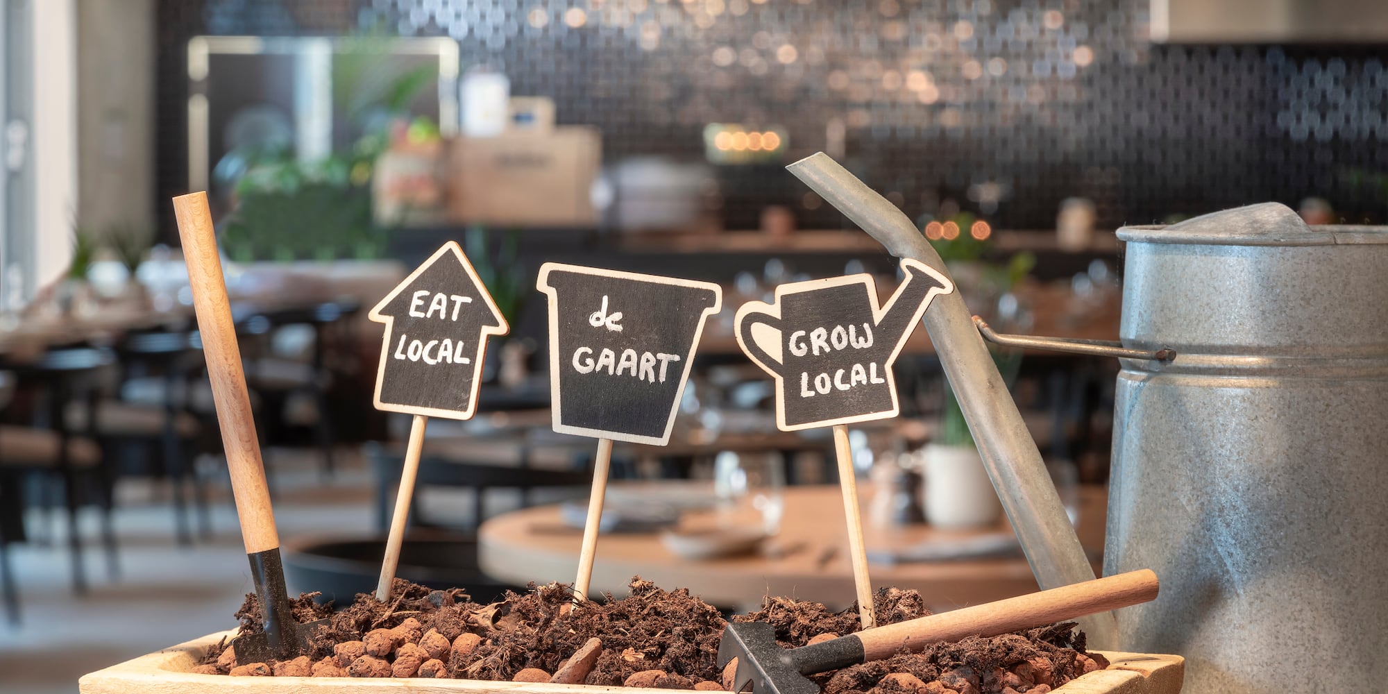 "Eat Local, Grow Local" signs in planter with garden tools, watering can.