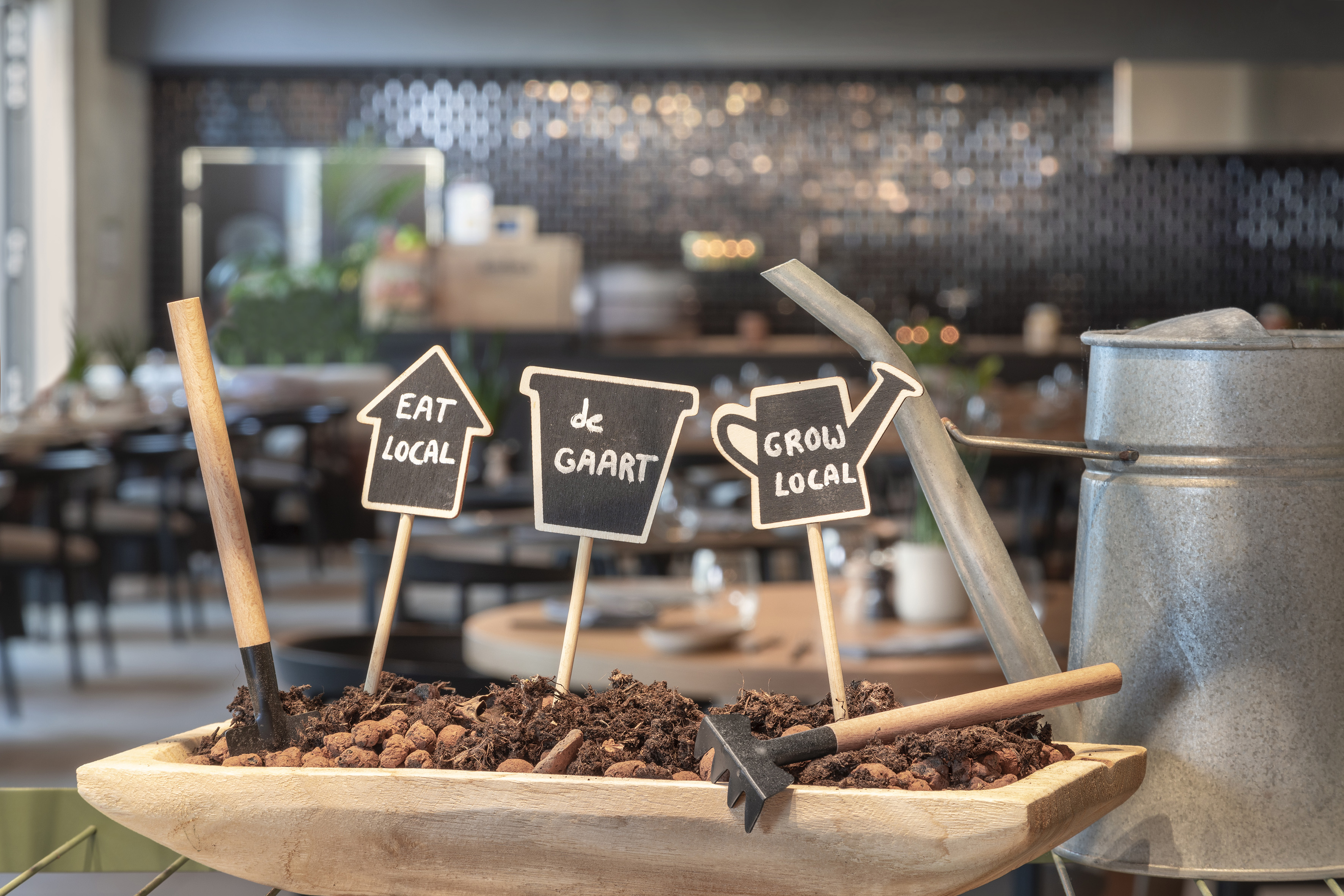 "Eat Local, Grow Local" signs in planter with garden tools, watering can.
