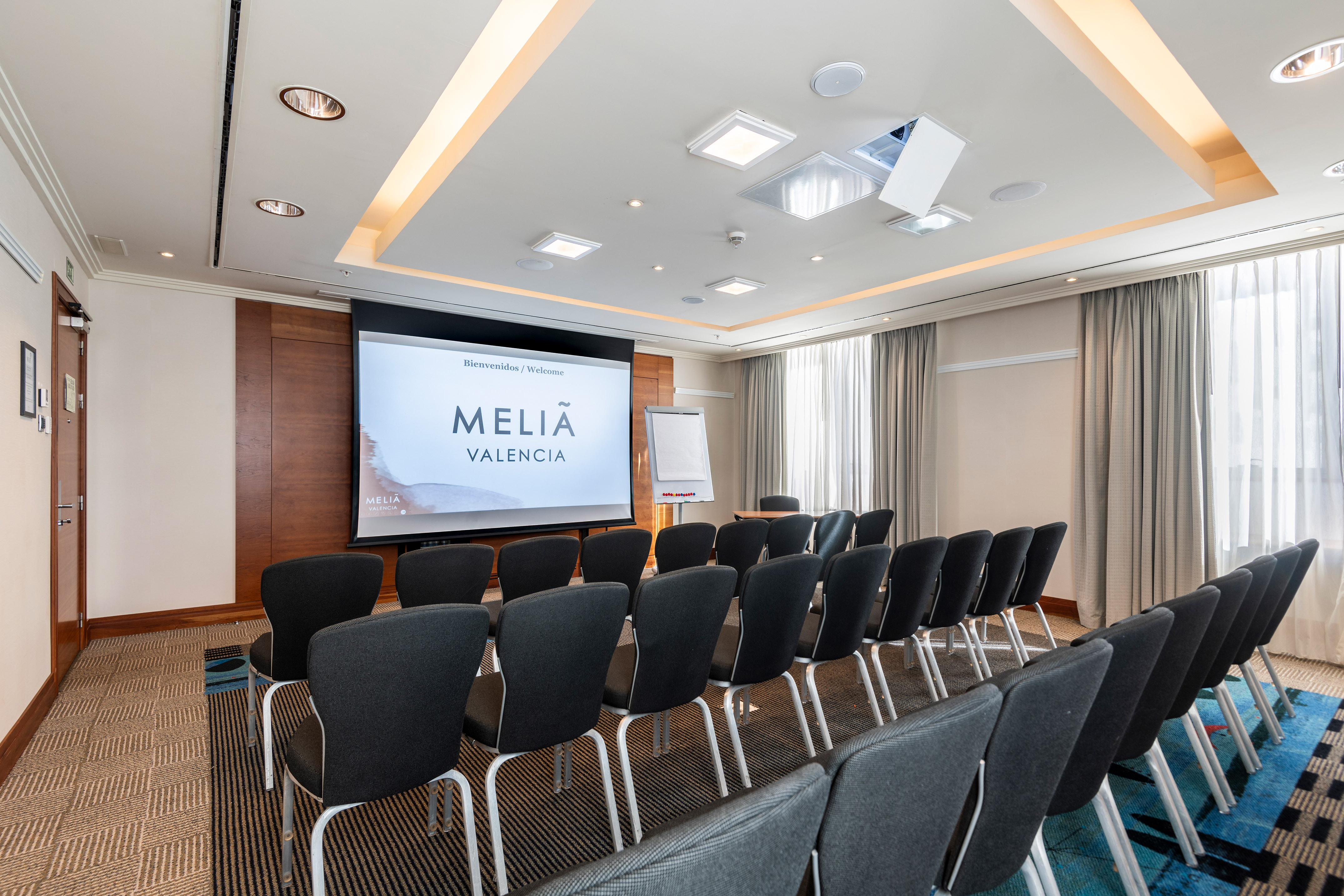 Meliá Valencia conference room with projection screen, rows of chairs, whiteboard.