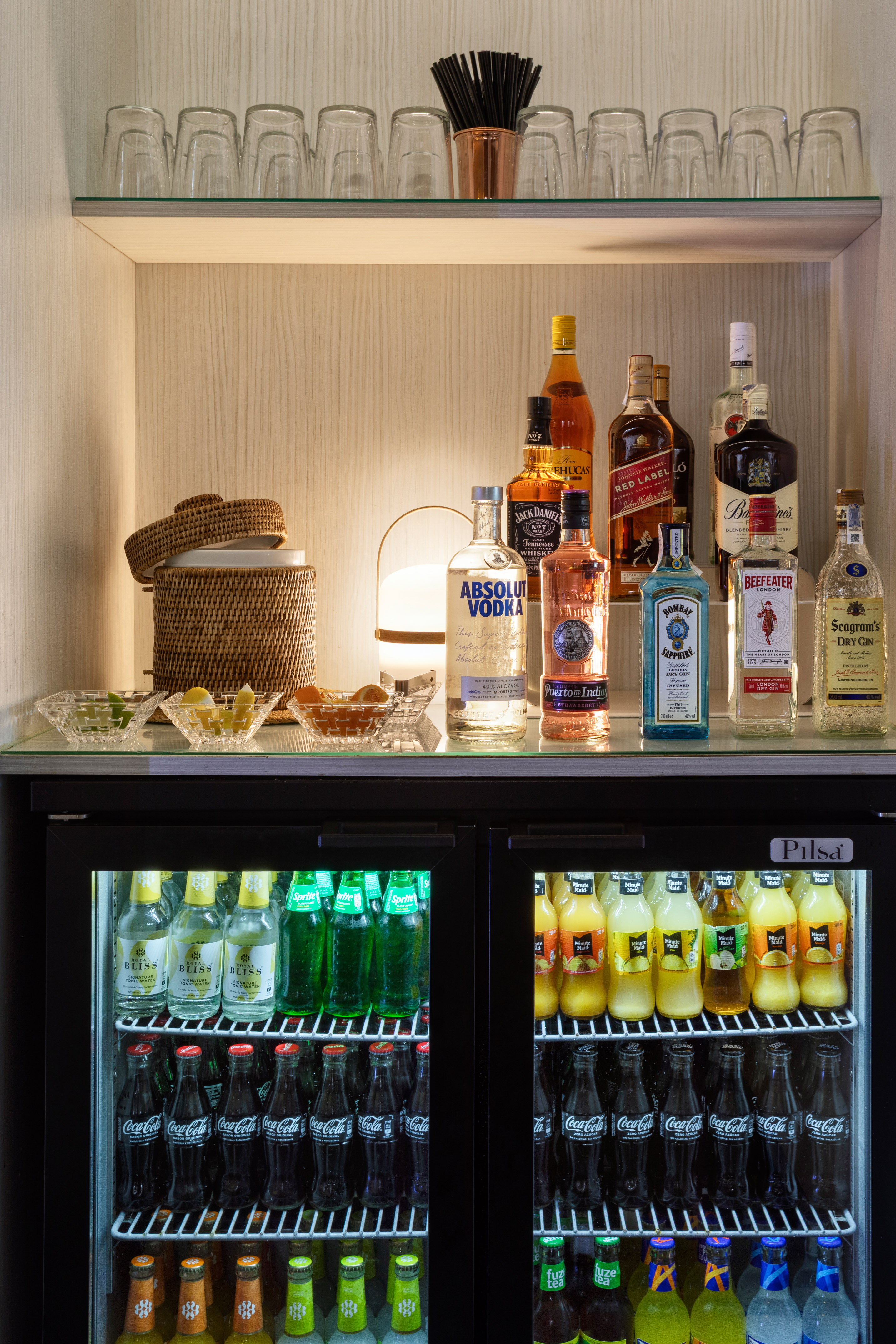 Hotel mini-bar stocked with liquor bottles, soft drinks, juices, and glassware.