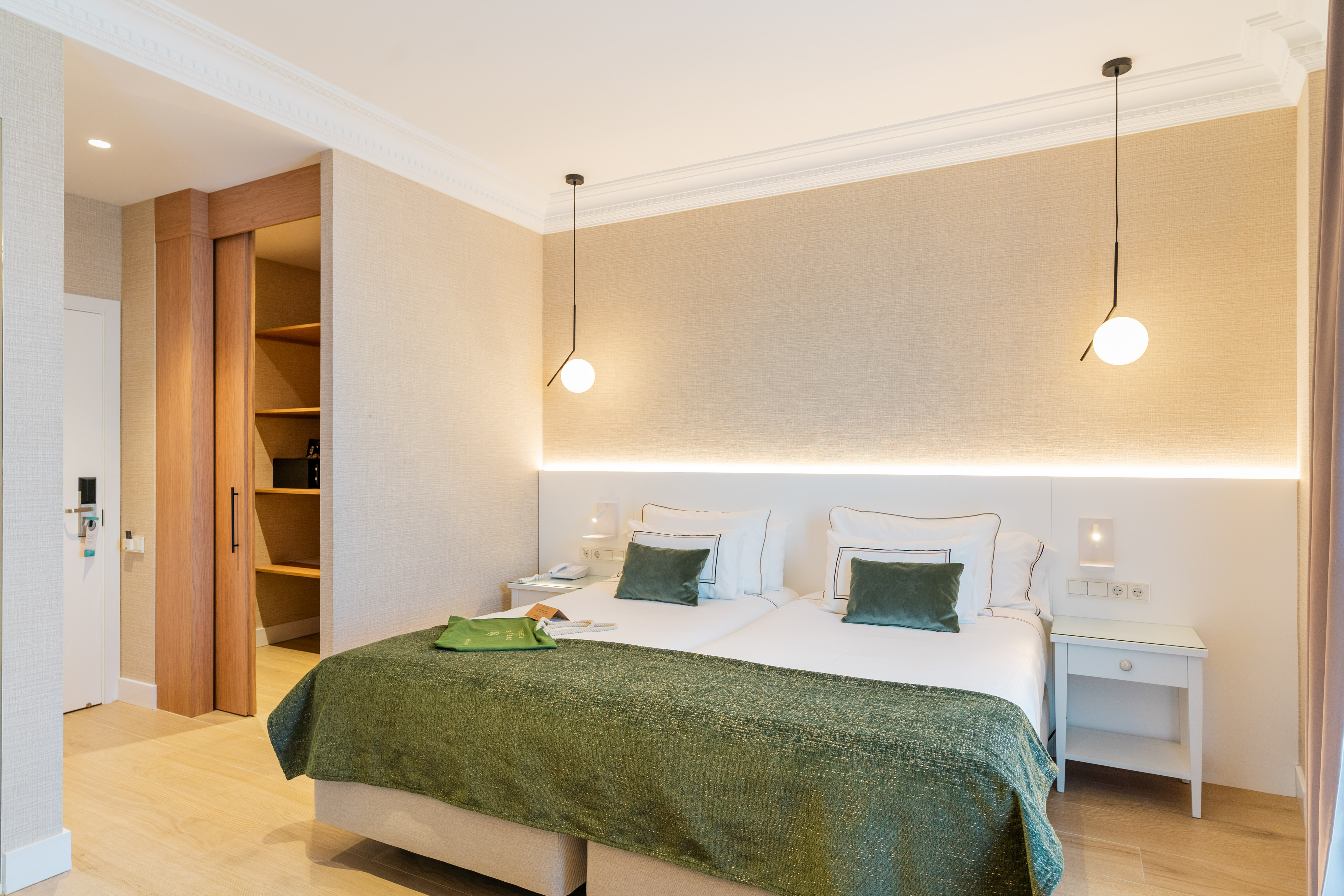 Modern hotel room with two beds, green bedding, and a built-in wooden closet.