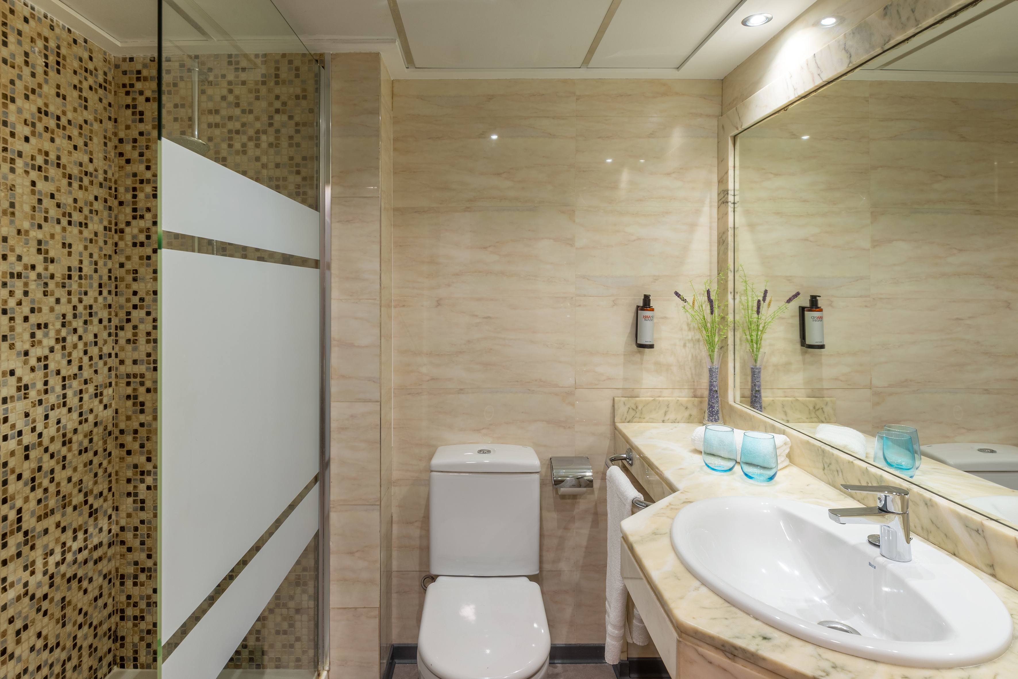 Modern hotel bathroom with mosaic shower, toilet, sink, and marble counter.