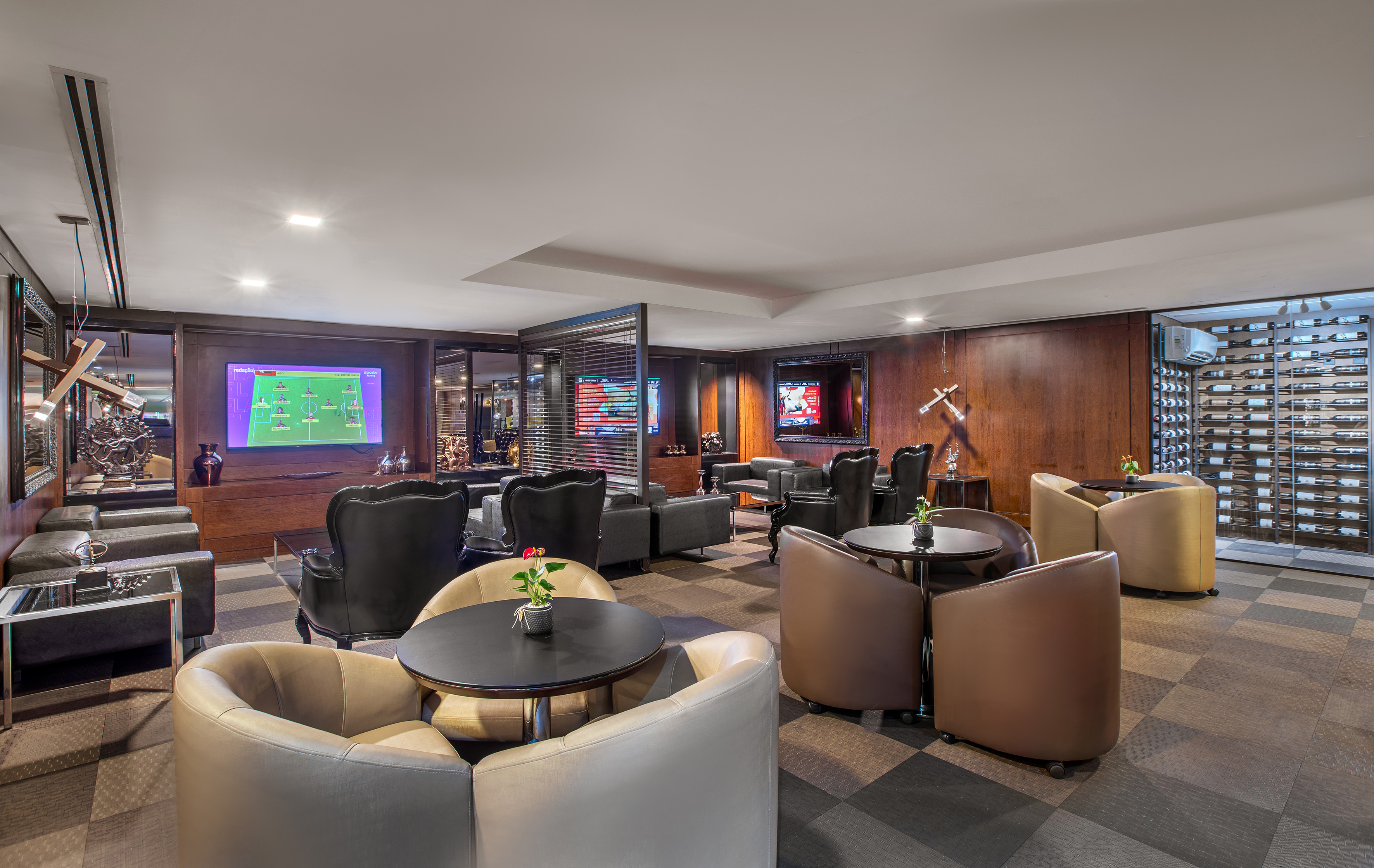 Elegant lounge bar with TVs, plush seating, dark wood panels, and a wine rack.