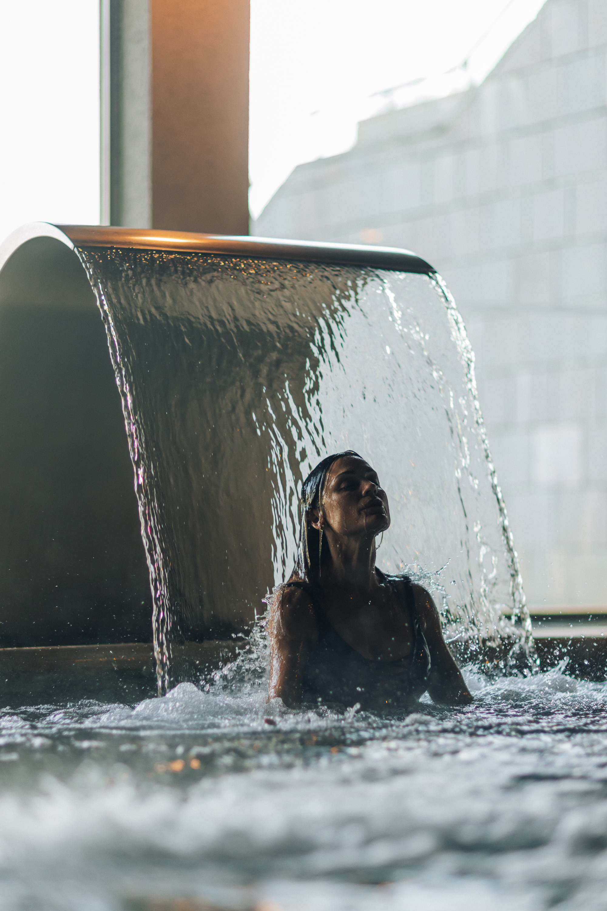 Woman in spa pool with cascading waterfall, head tilted back in relaxation.