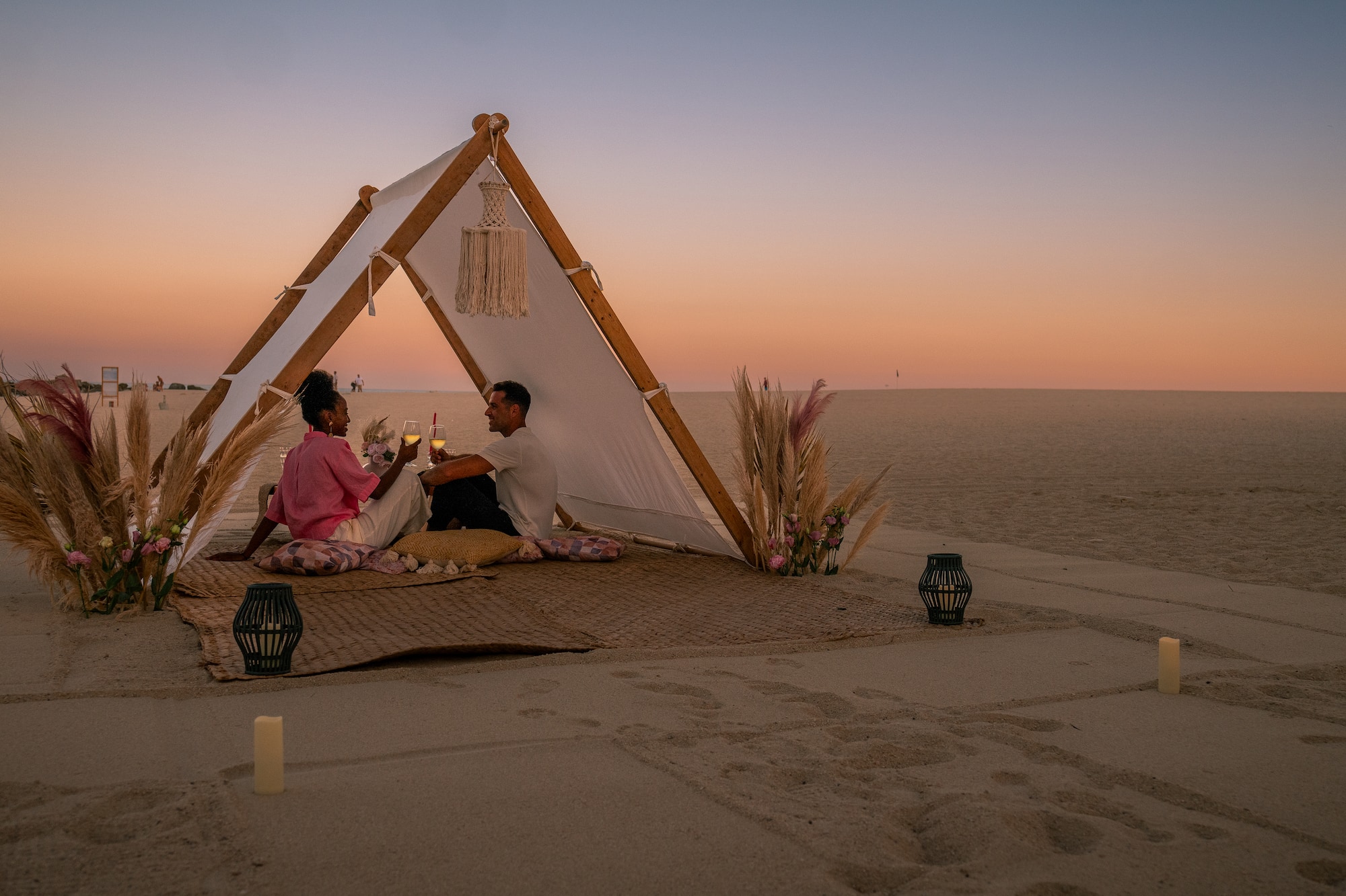 a man and woman sitting on a blanket in the sand