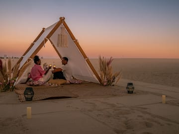 a man and woman sitting on a blanket in the sand