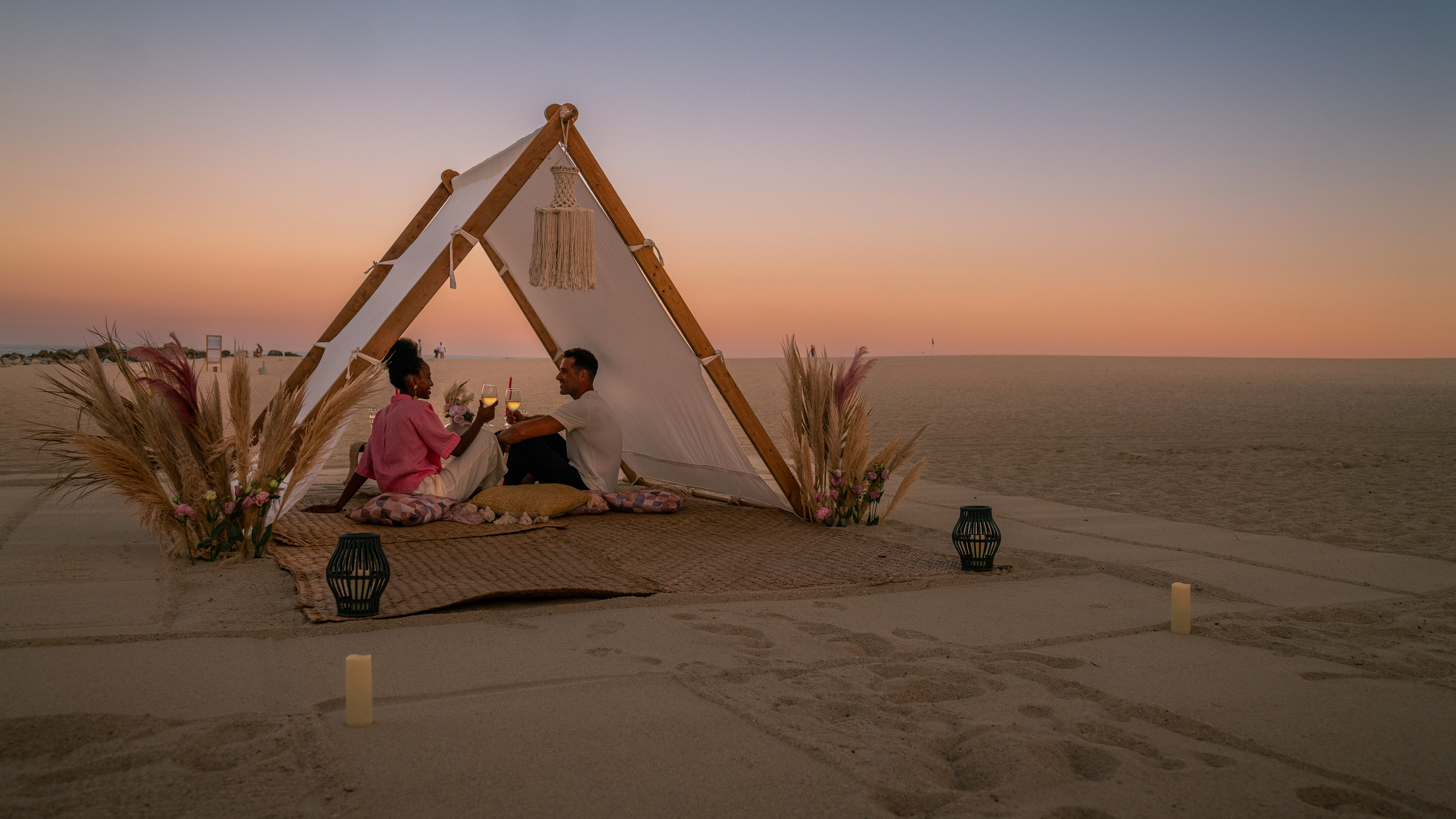 a man and woman sitting on a blanket in the sand