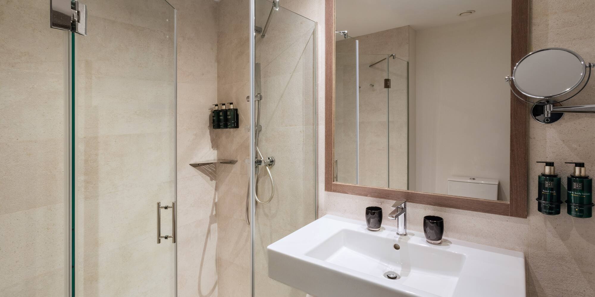 Modern bathroom with glass shower enclosure, white sink, and large framed mirror.