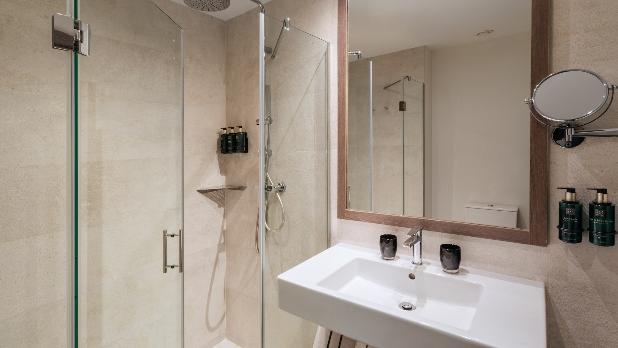Modern bathroom with glass shower enclosure, white sink, and large framed mirror.
