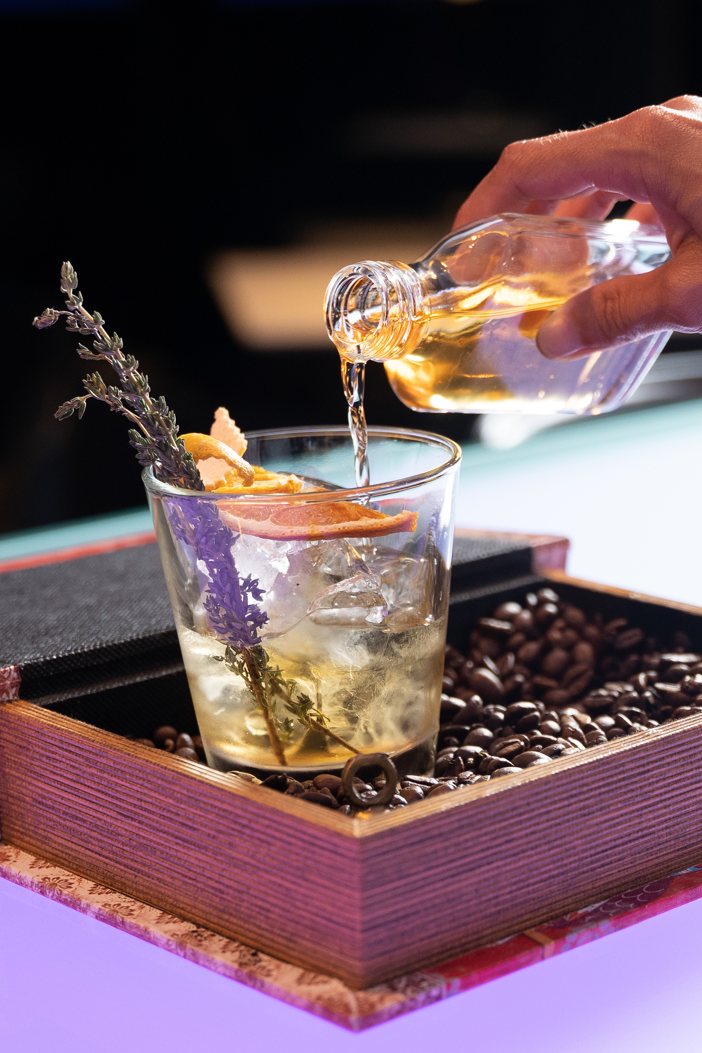 Pouring liquor into lavender-orange cocktail with ice, on coffee beans. - Twist Bar - Innside Dresda, Dresda