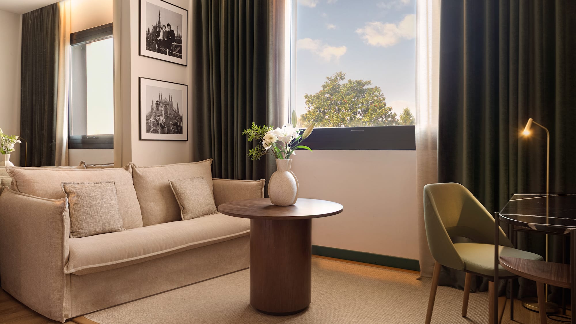 Modern hotel living space with beige sofa, window, wood table, framed art.