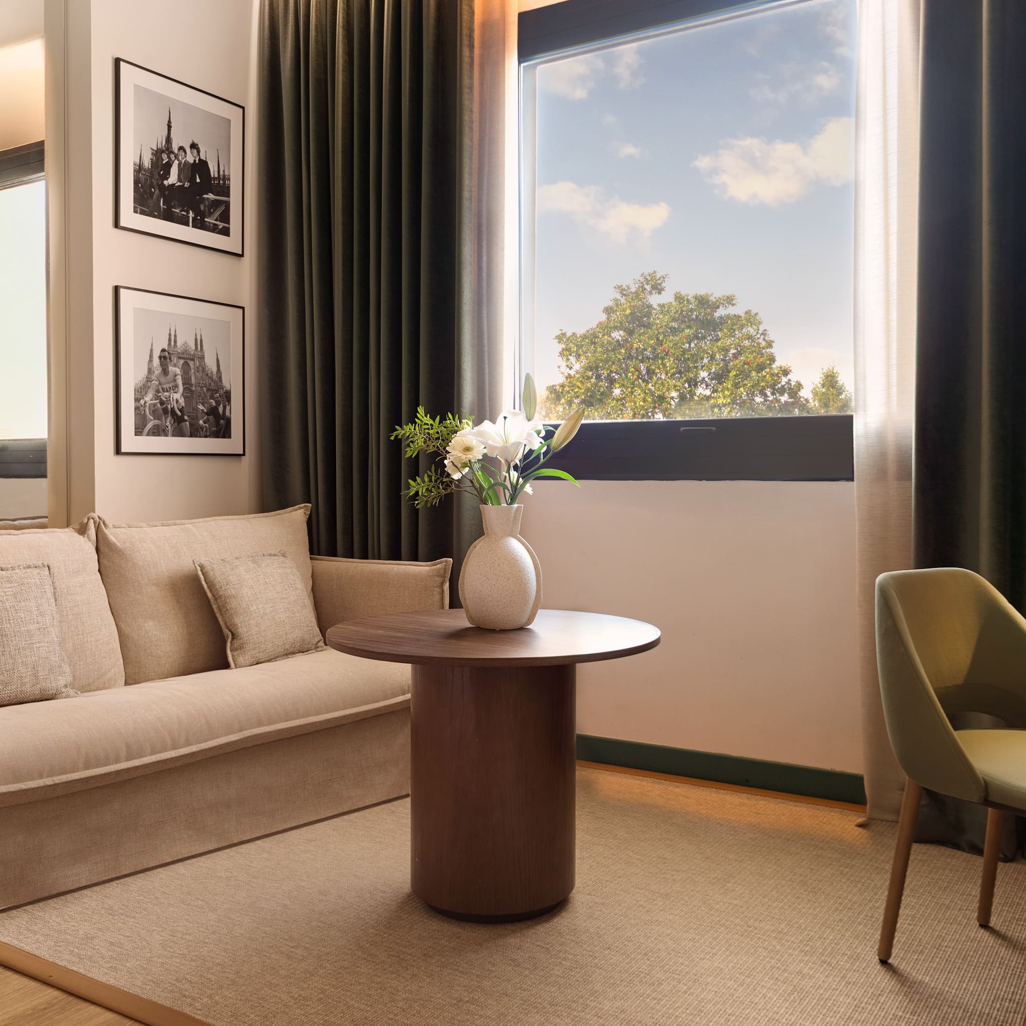 Modern hotel living space with beige sofa, window, wood table, framed art.