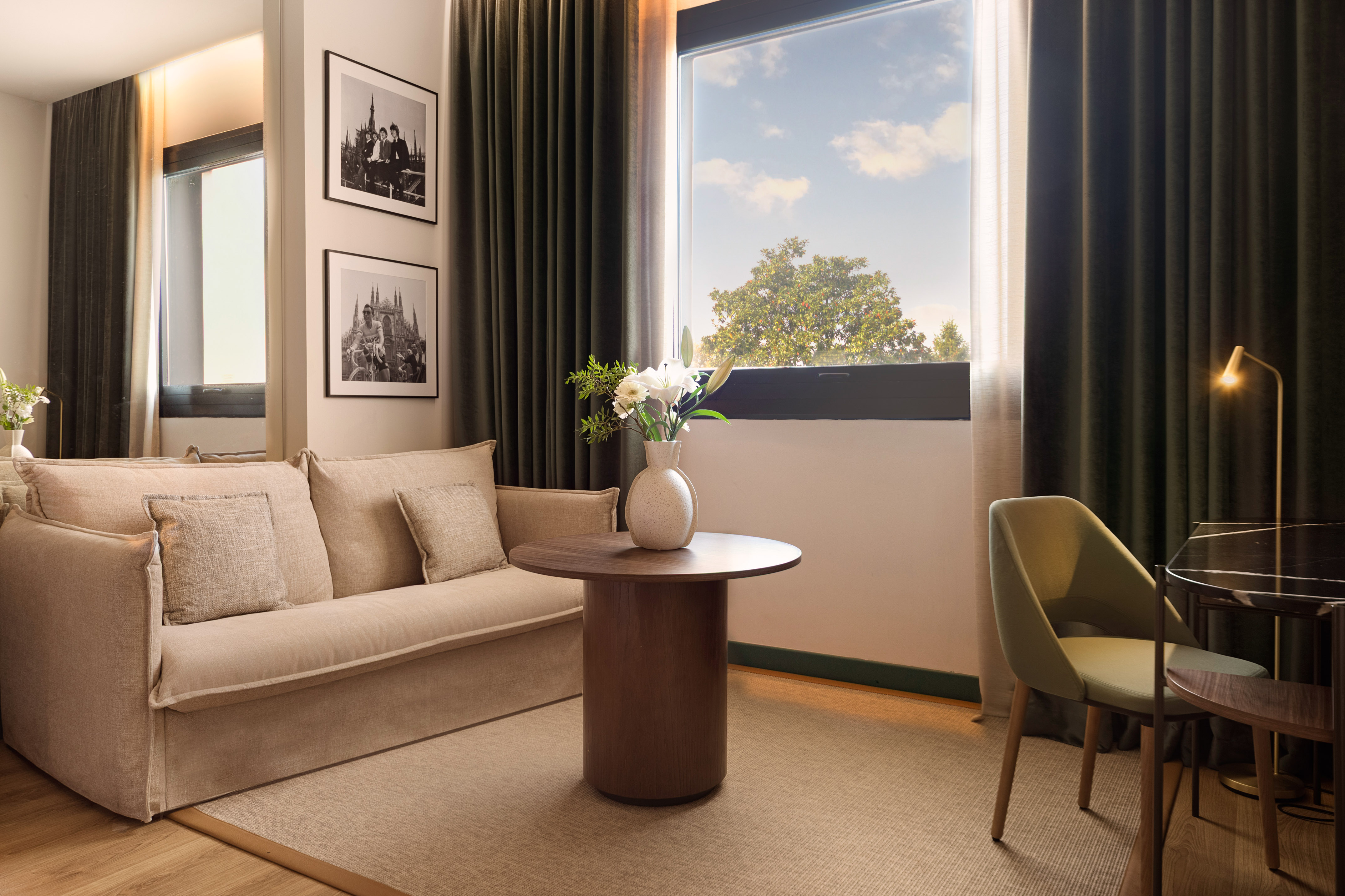 Modern hotel living space with beige sofa, window, wood table, framed art.