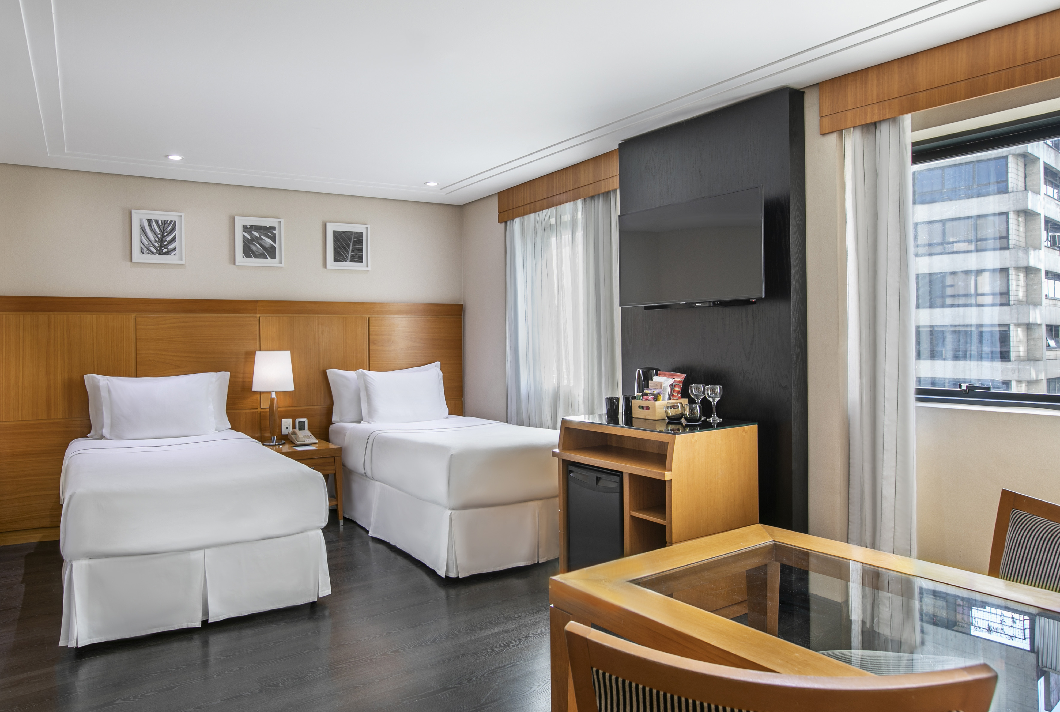 Modern hotel room with two twin beds, minibar, TV, and city view.
