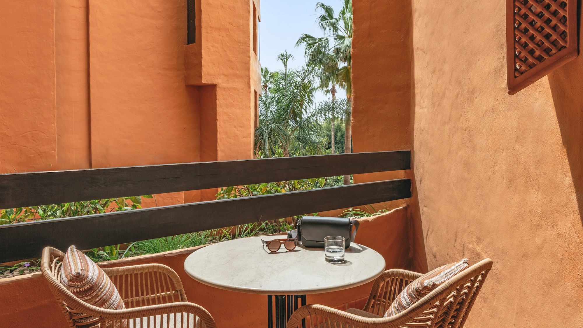 Terracotta balcony with wicker chairs, table, sunglasses, and palm trees.