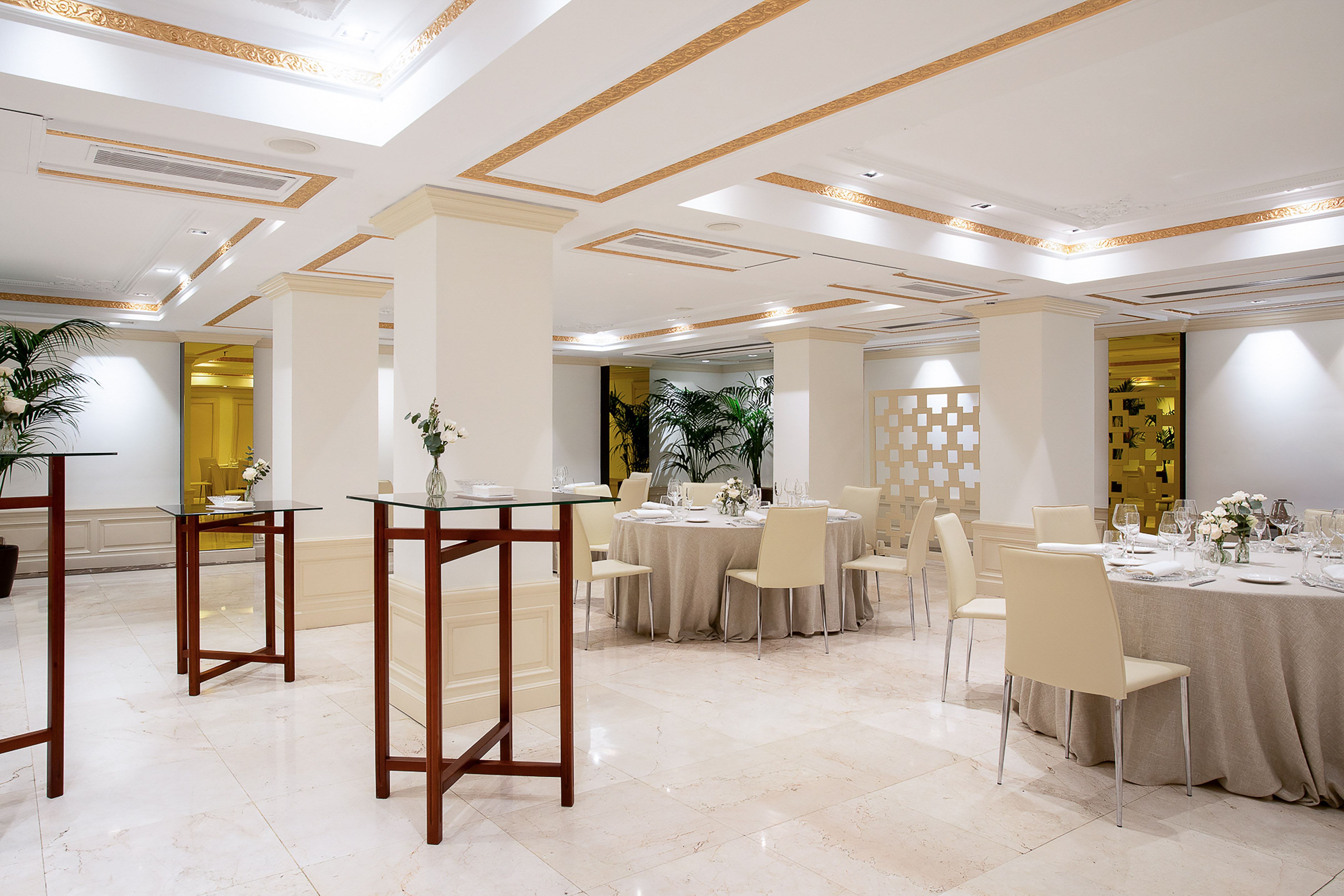 Elegant hotel event room with set dining tables, gold trim, and marble floor.