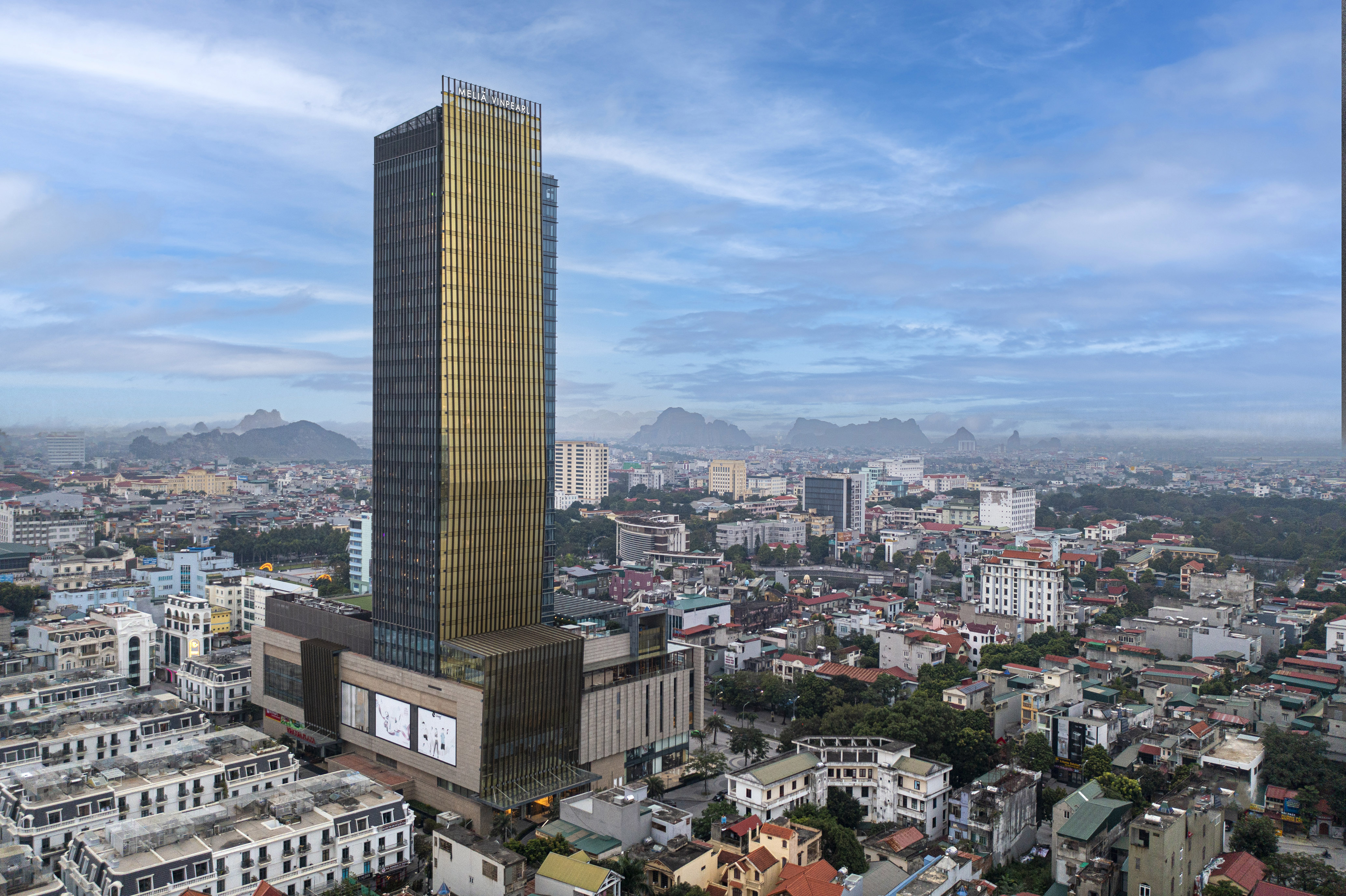 Melia Vinpearl hotel skyscraper over city and misty mountains.