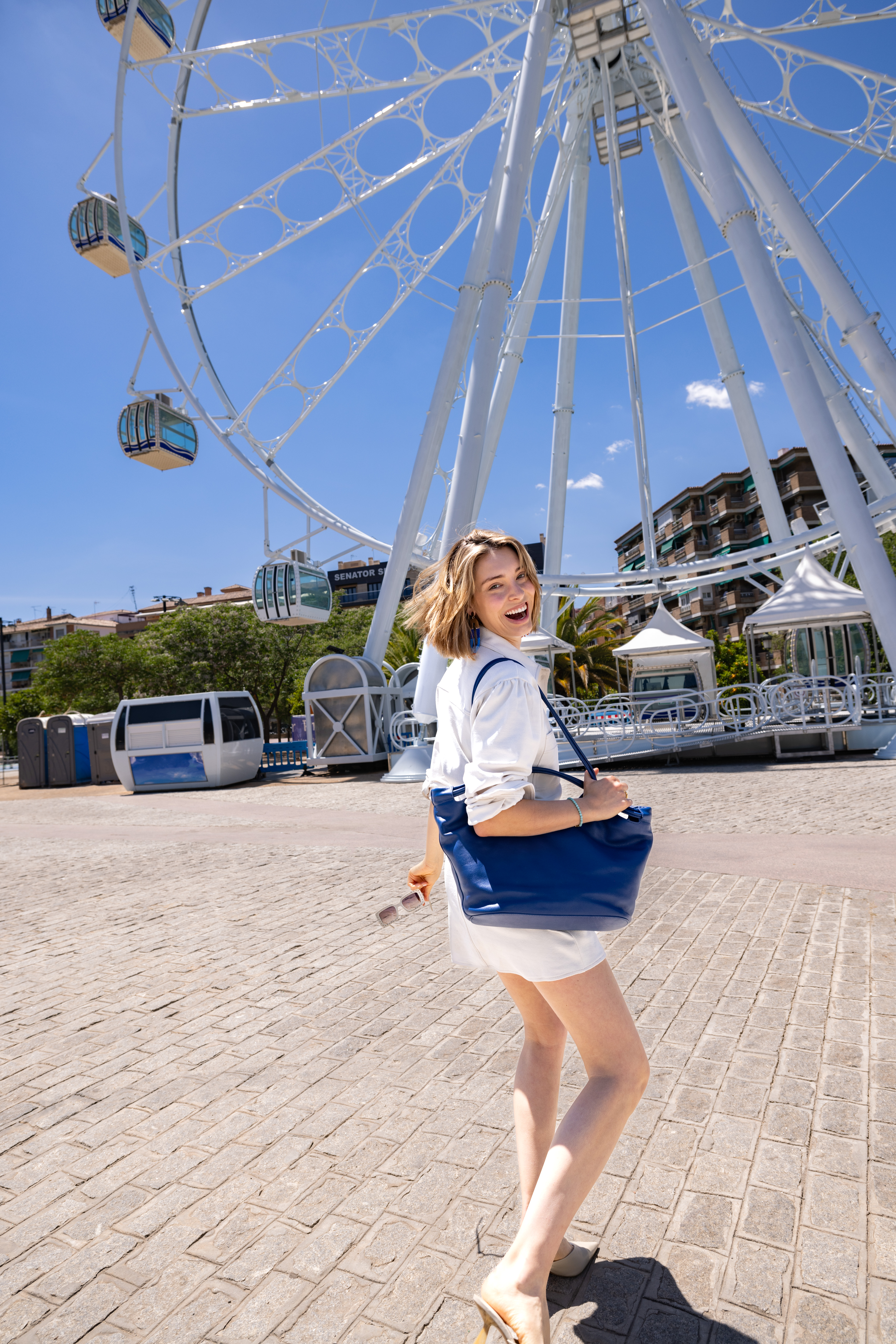 a woman in white dress and blue purse standing in front of a ferris wheel