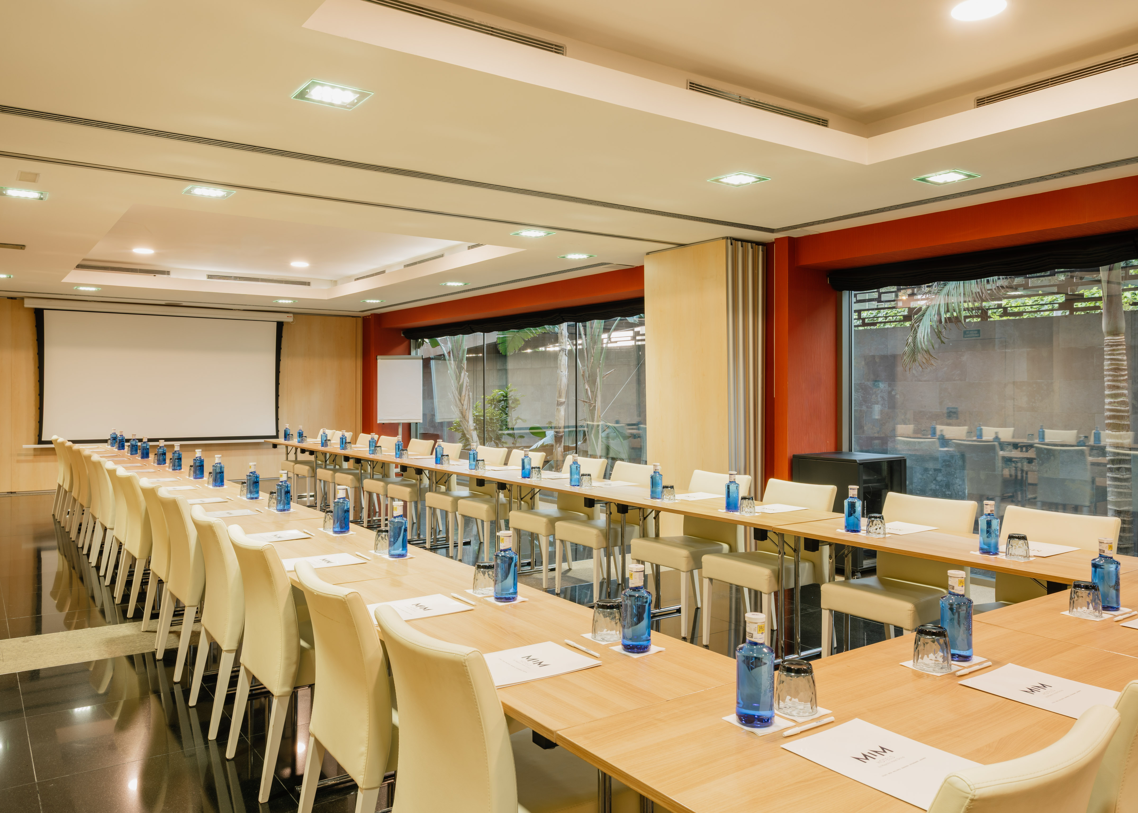 Hotel conference room with U-shaped tables, projector, and garden view.