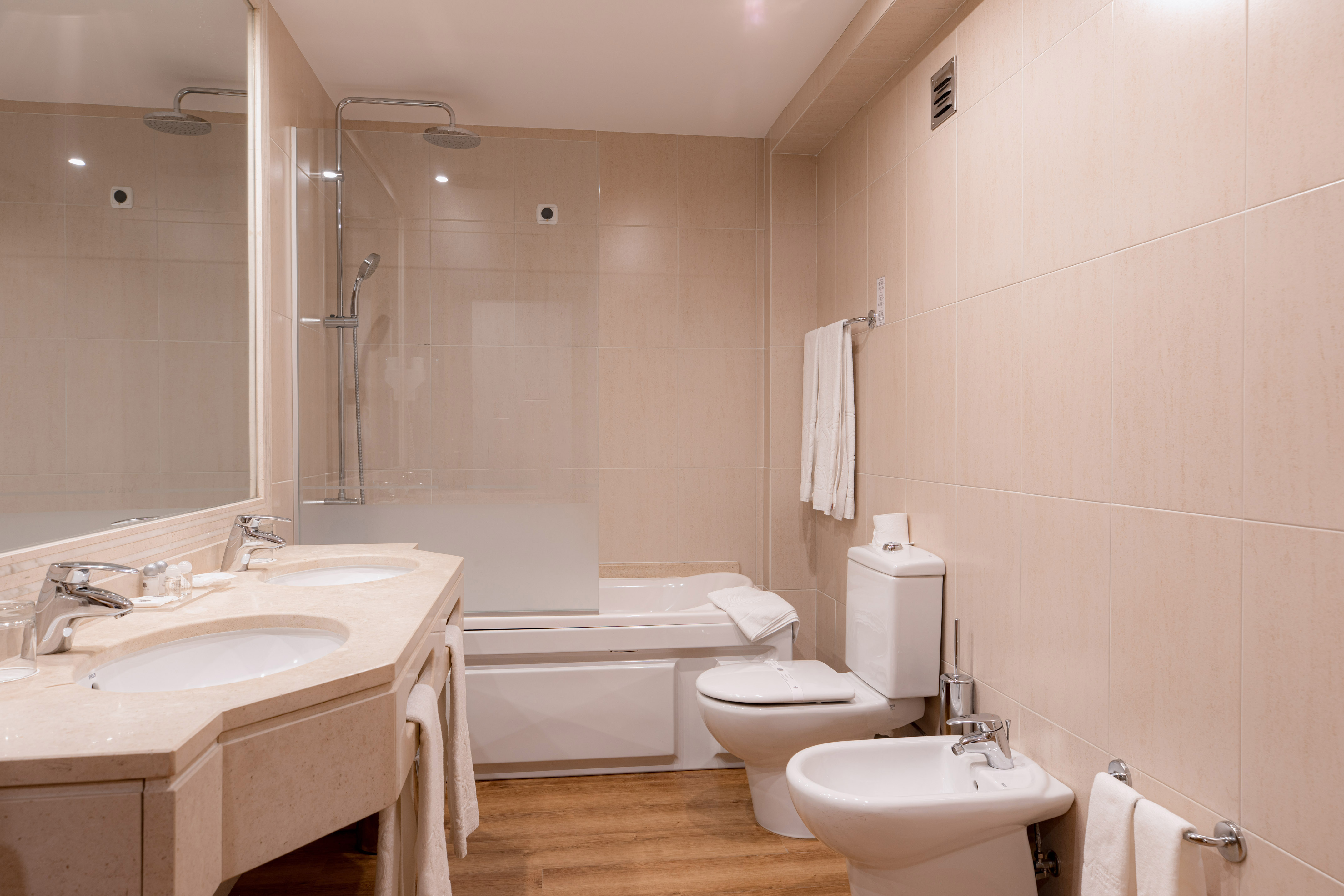 Hotel bathroom with double vanity, shower-tub, toilet, and bidet.