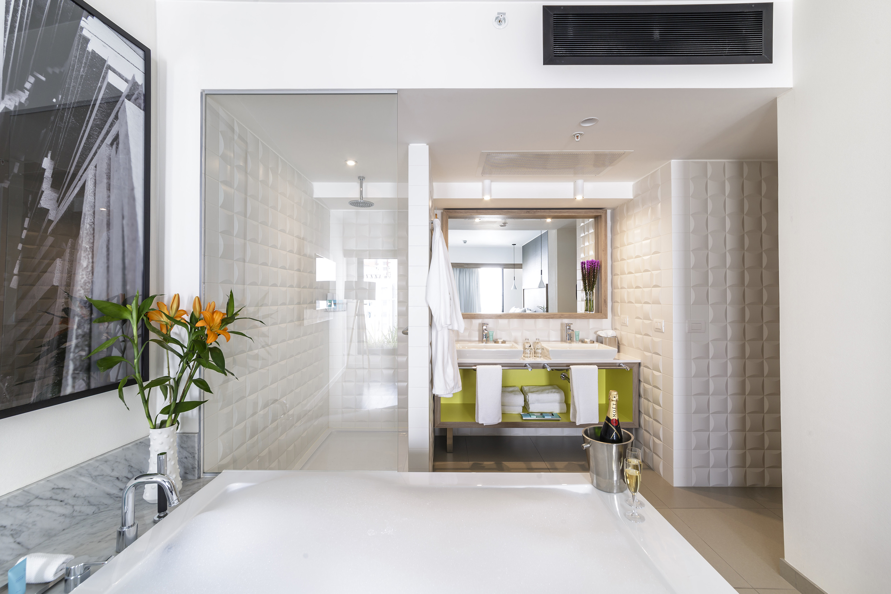 Modern luxury hotel bathroom: deep tub, glass shower, double vanity, champagne.
