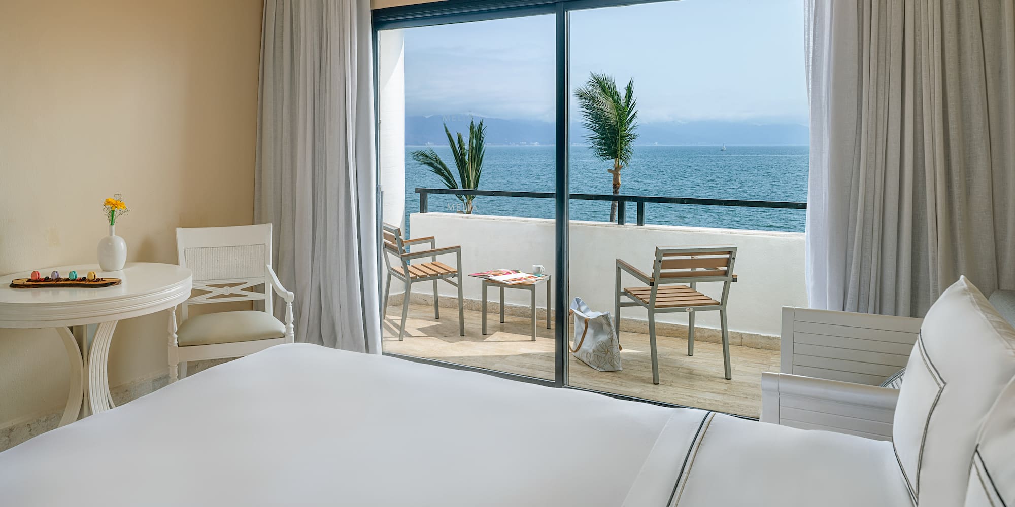 Ocean view hotel room with balcony overlooking the sea, bed, and chairs.