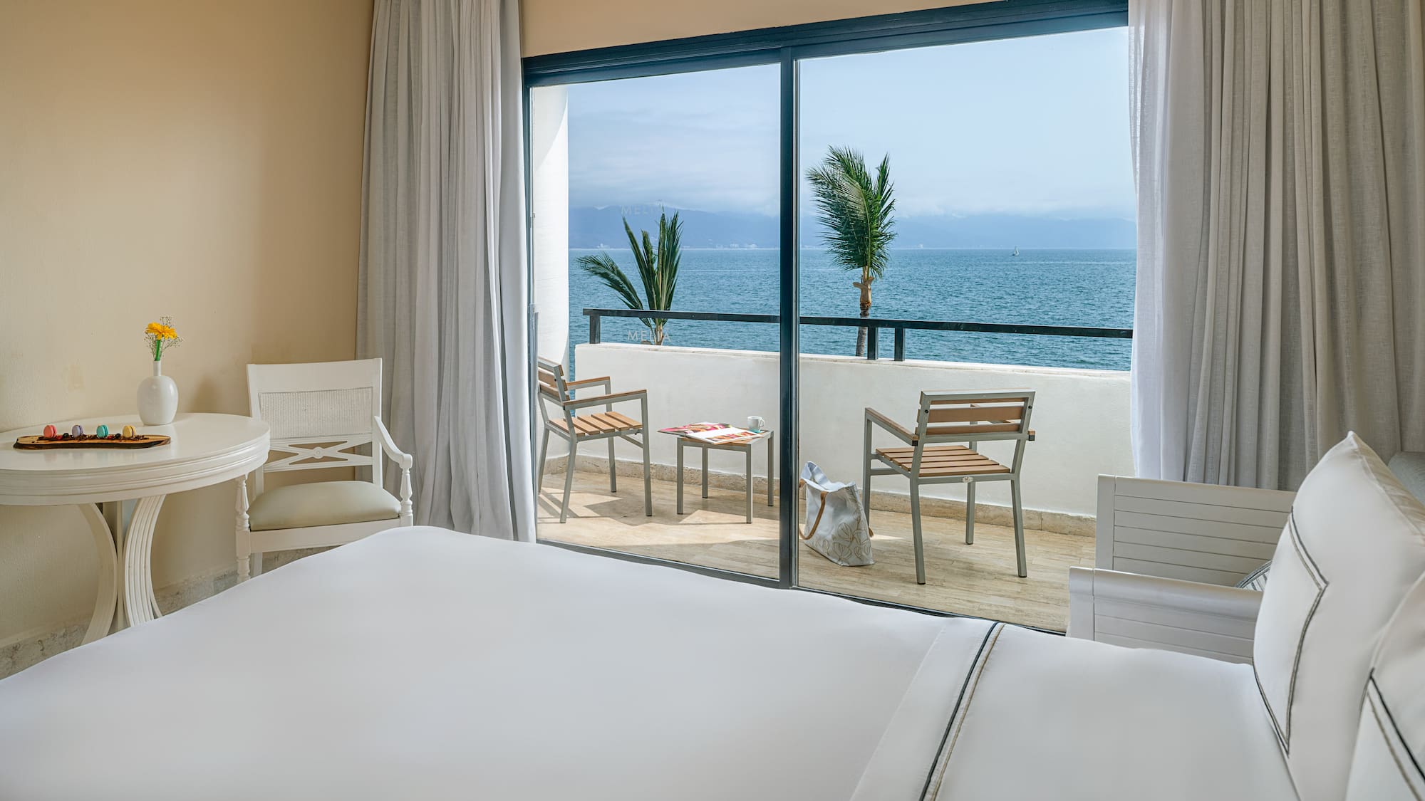 Ocean view hotel room with balcony, tropical sea, and palm trees.