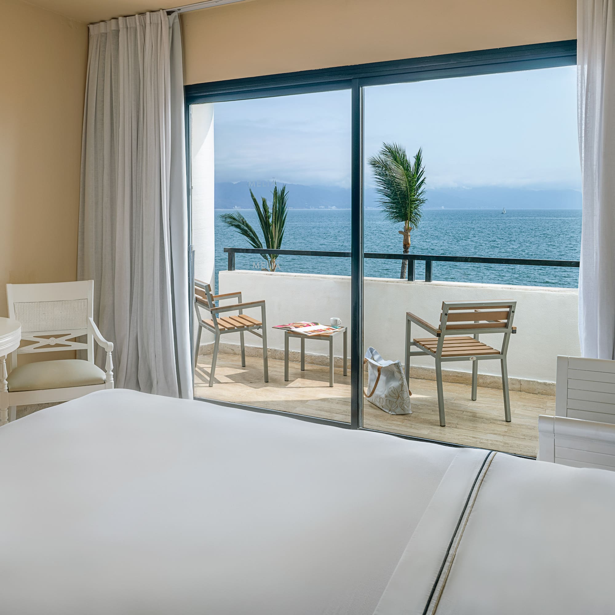Ocean view hotel room with balcony, tropical sea, and palm trees.