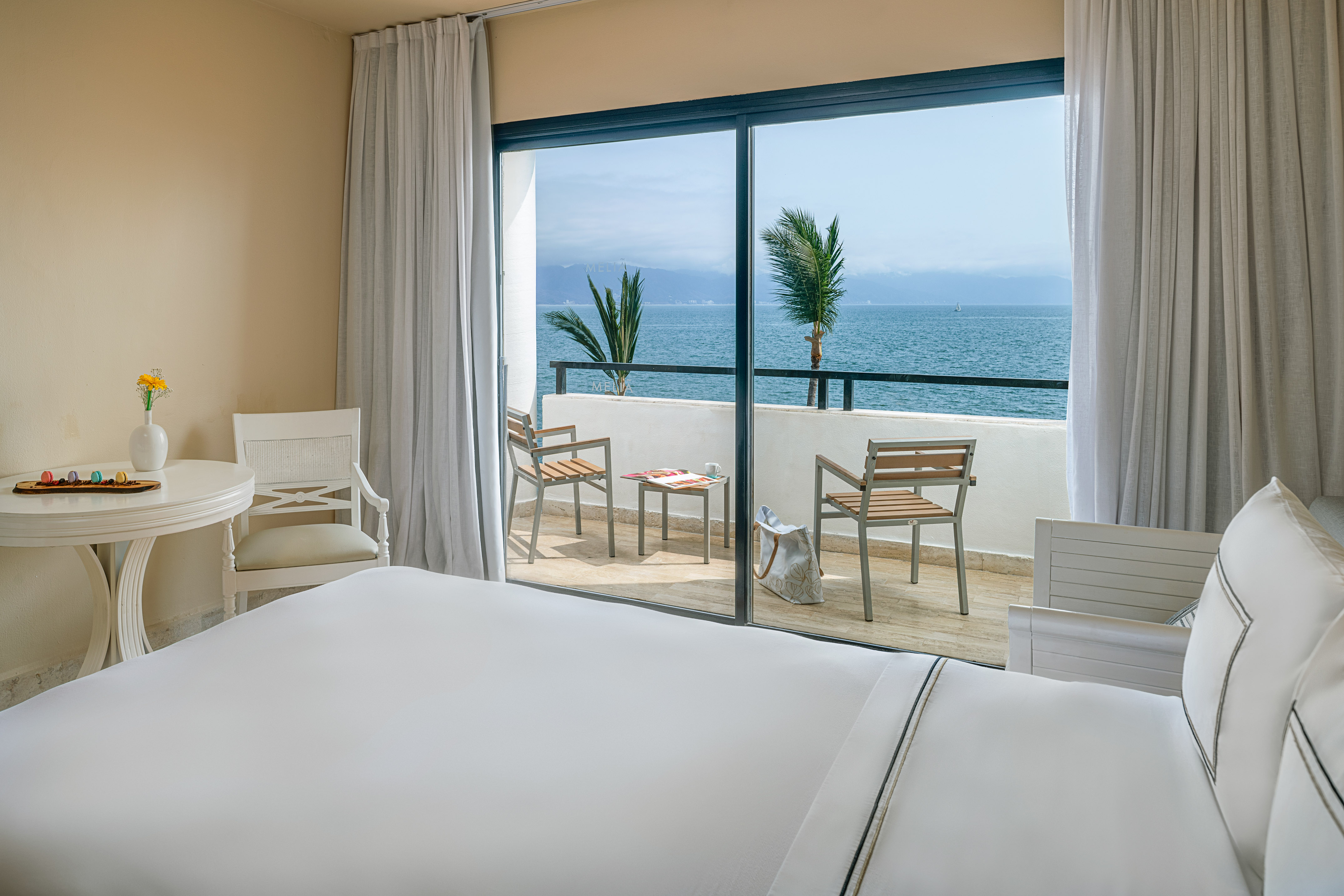 Ocean view hotel room with balcony overlooking the sea, bed, and chairs.