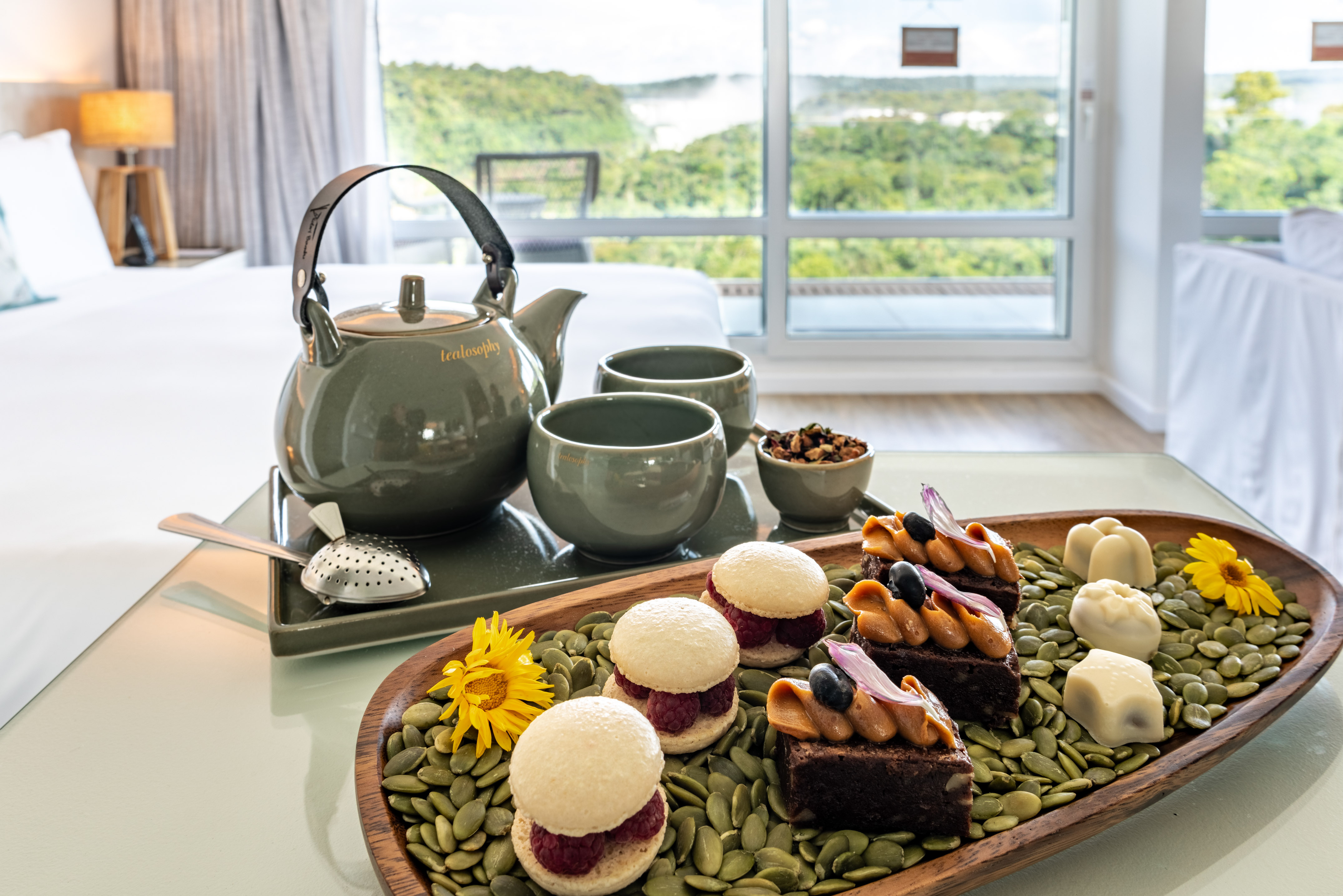 Tea set, gourmet desserts with macarons and brownies, hotel room forest view.