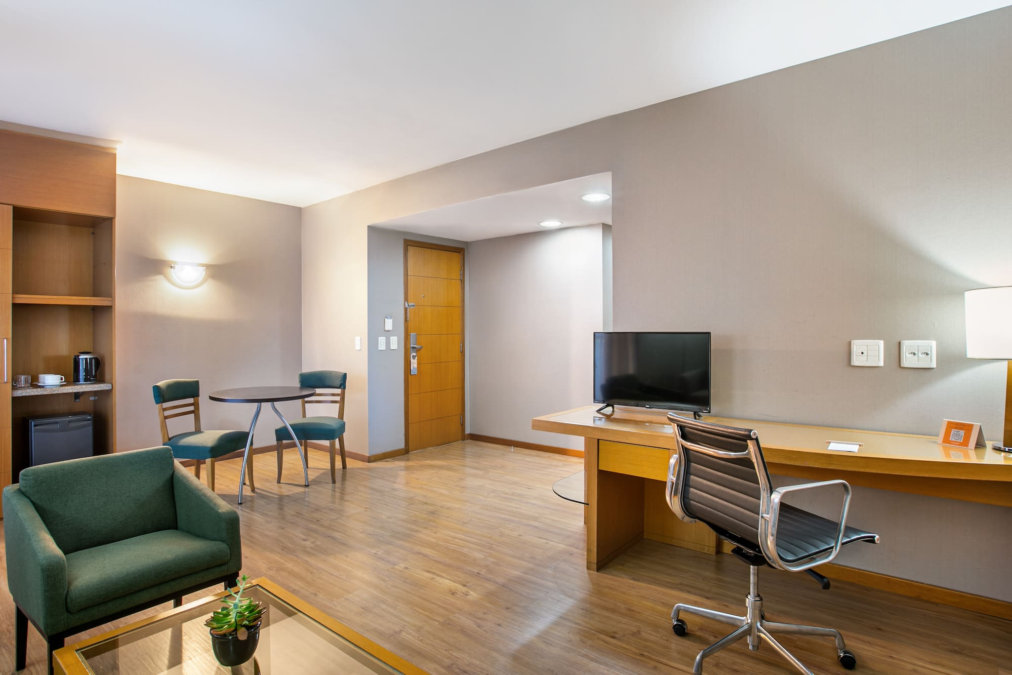 Contemporary hotel suite with living area, desk, and kitchenette.