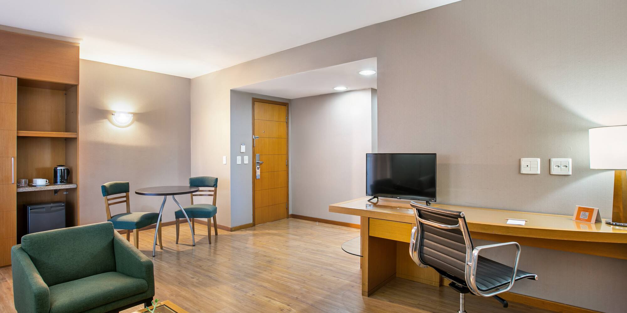 Contemporary hotel suite with living area, desk, and kitchenette.