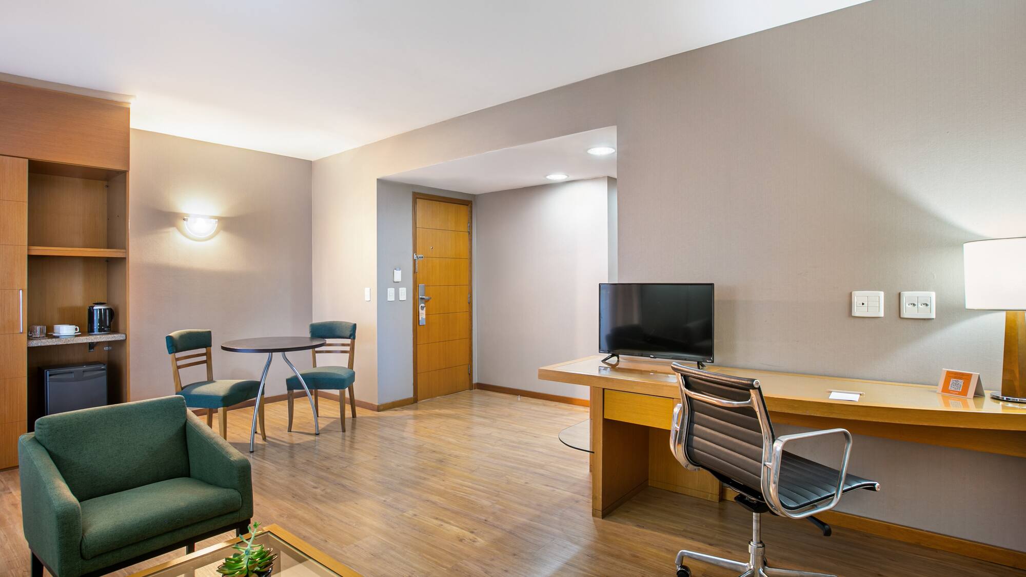 Contemporary hotel suite with living area, desk, and kitchenette.