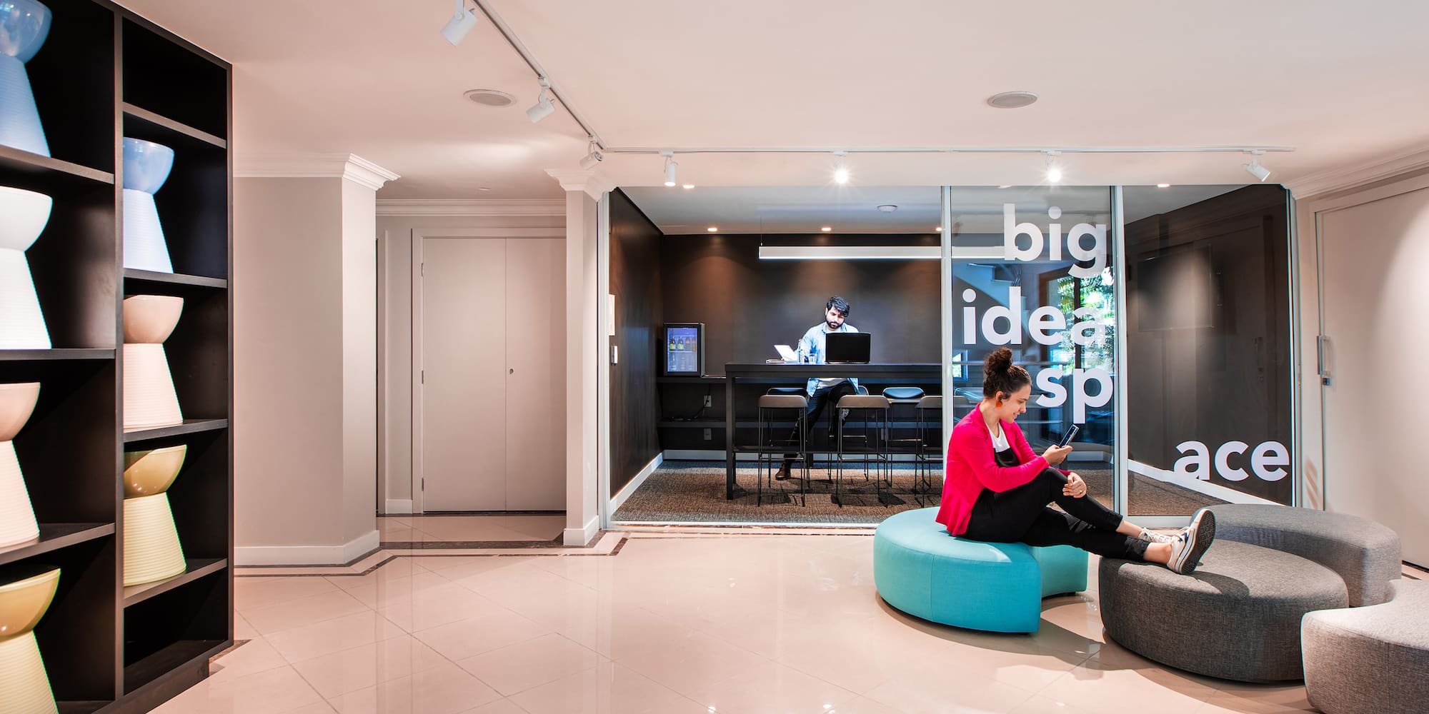 a woman sitting on a blue pouf in a room with a man and a desk