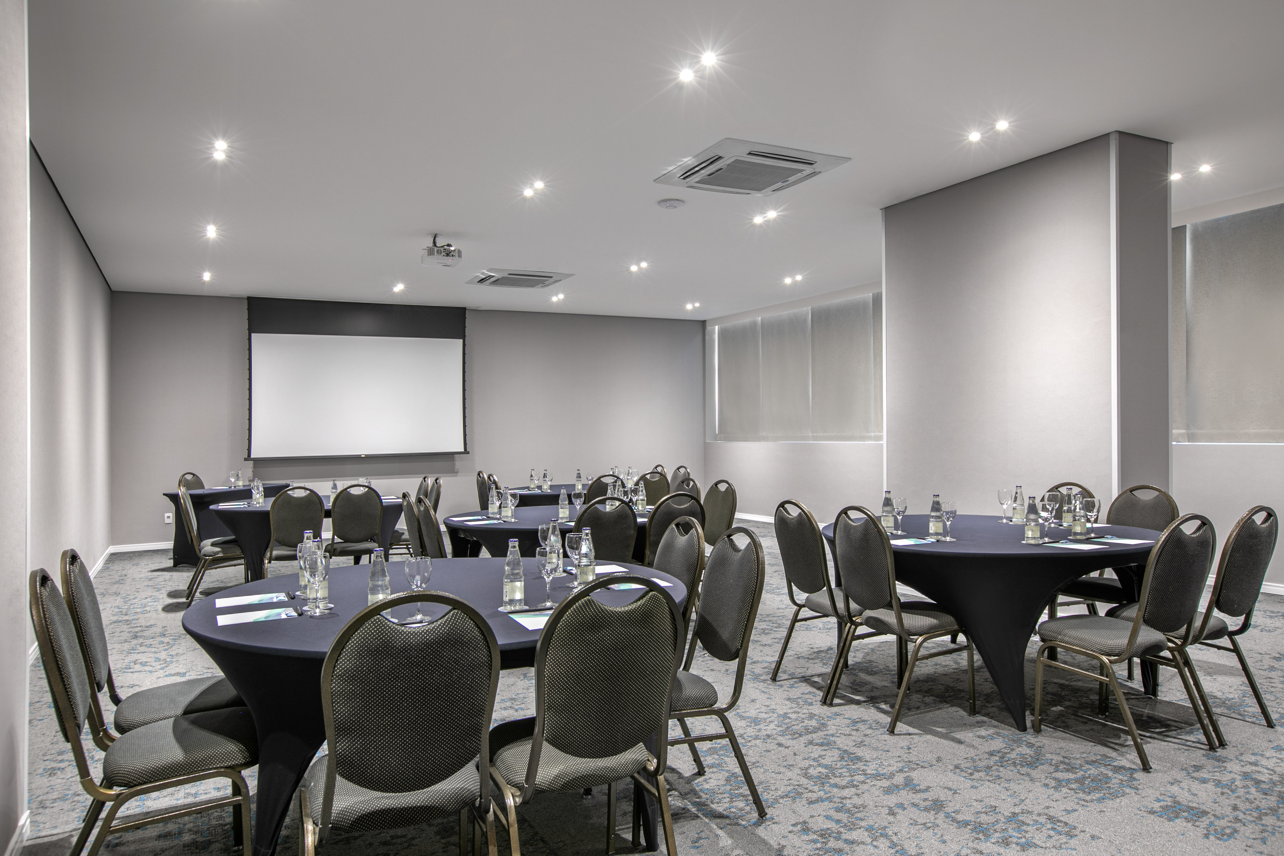 Modern conference room with round tables, projector screen, set for an event.