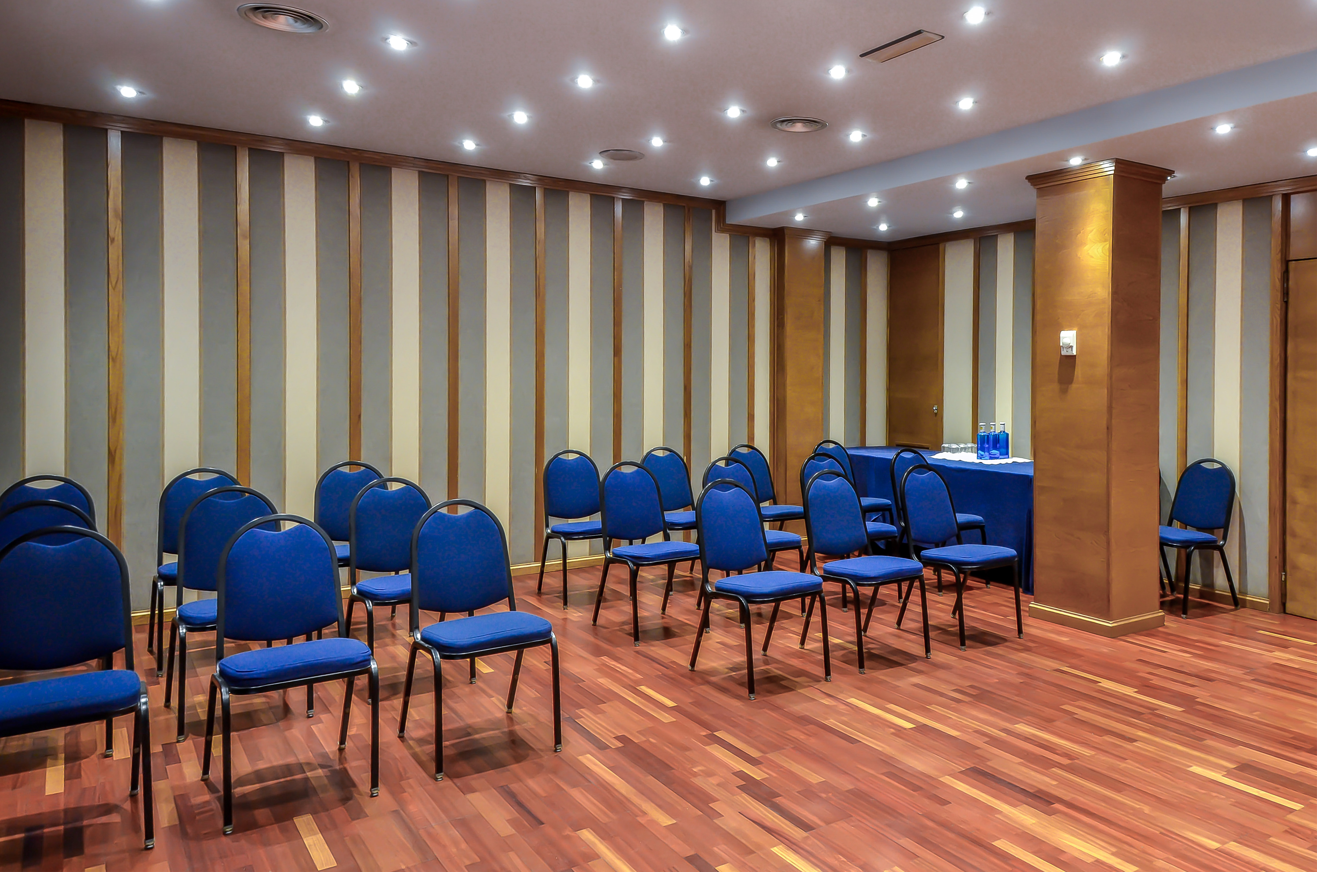 Empty conference room with blue chairs, wood flooring, and presentation table.