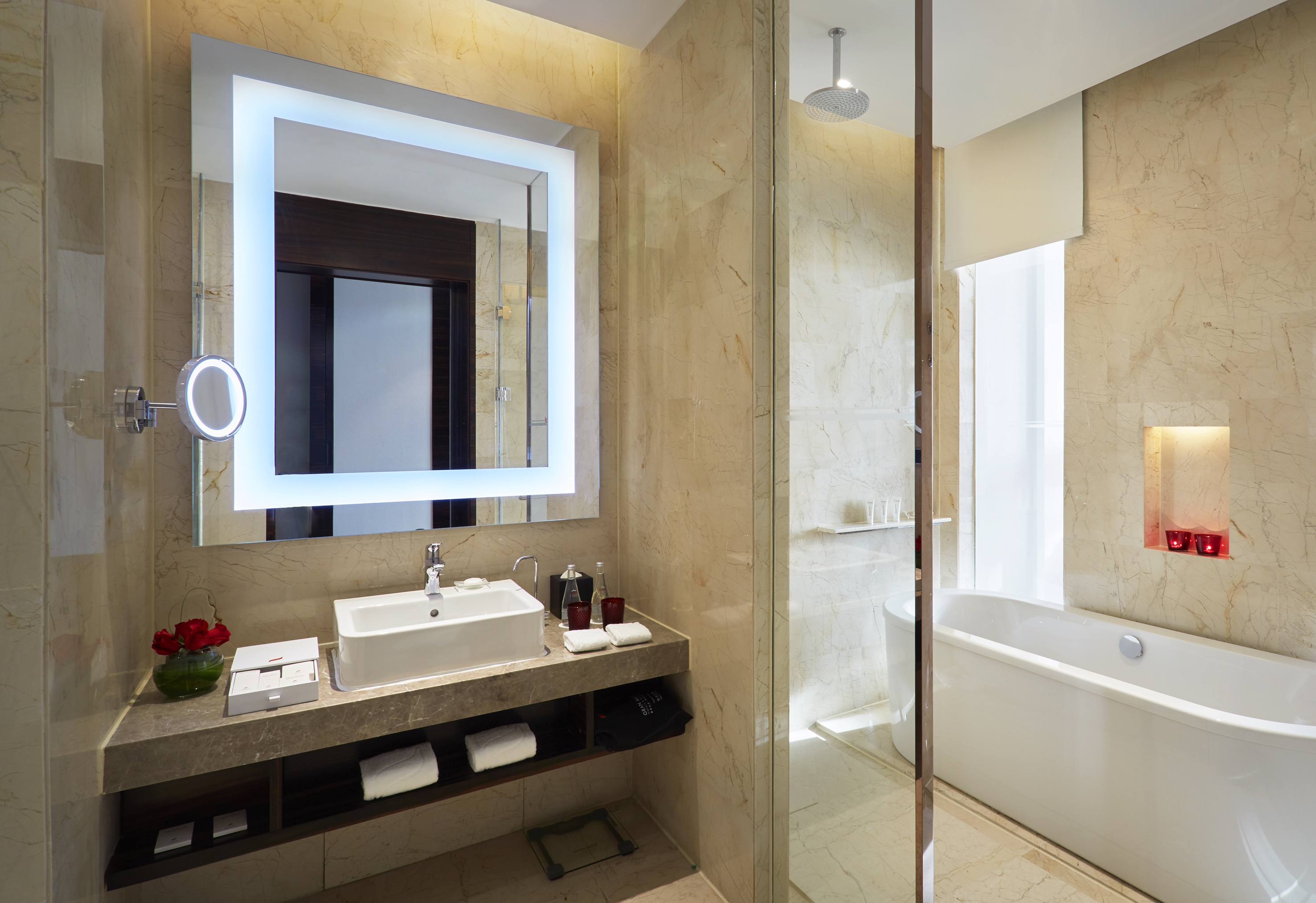 Modern marble bathroom with lighted mirror, vanity, bathtub, and shower.