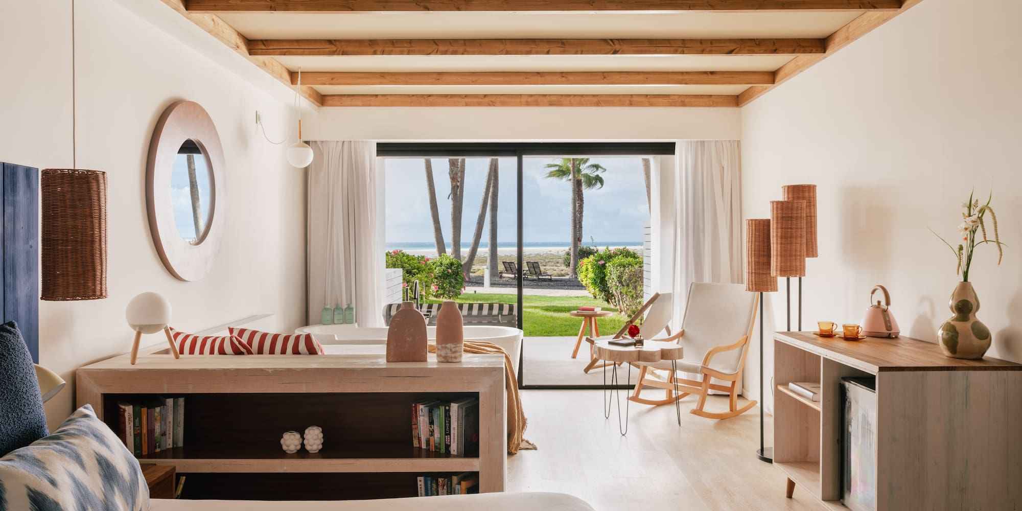Tropical hotel room with ocean view, palm trees, wooden beams, and coastal decor.