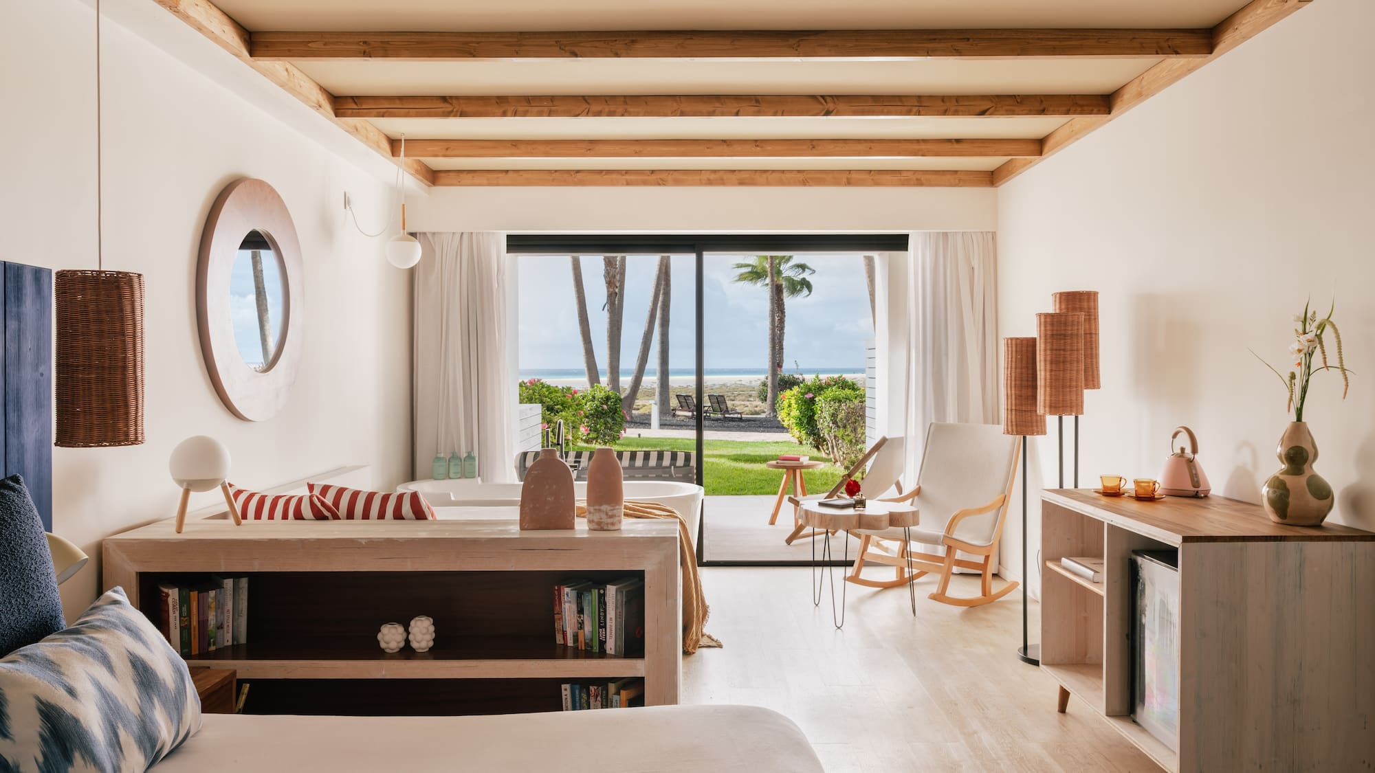 Tropical hotel room with ocean view, palm trees, wooden beams, and coastal decor.