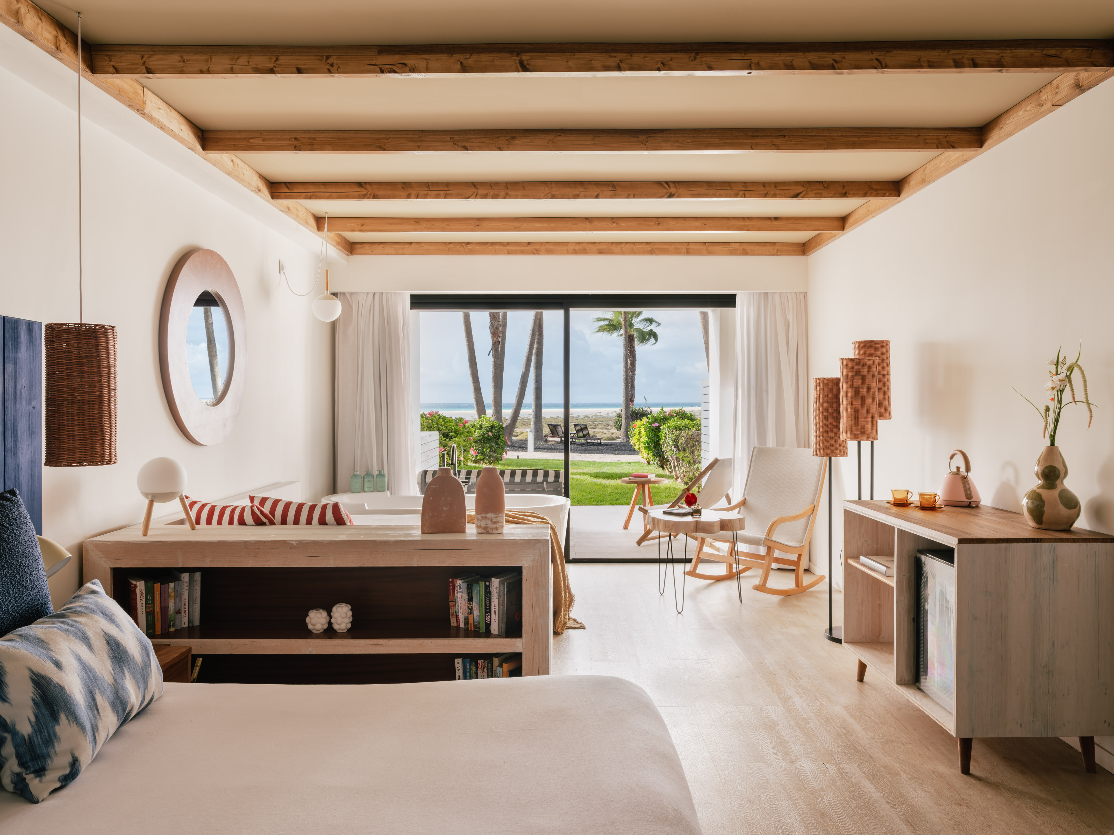Oceanfront hotel room with modern decor, beach view, and exposed wood beams.