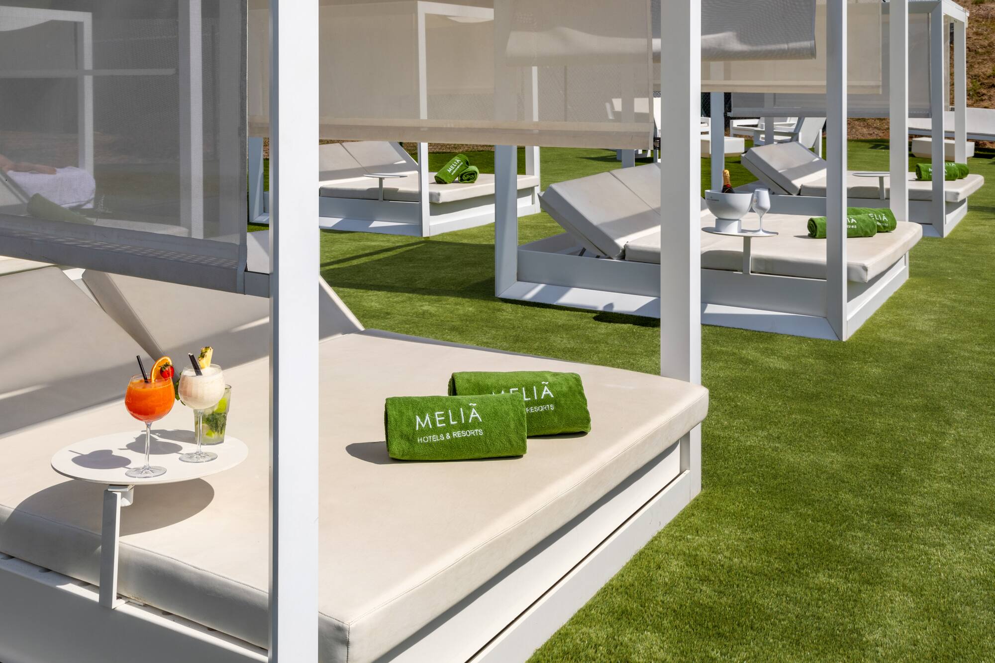 Meliá resort cabanas on green turf with cocktails and branded towels.