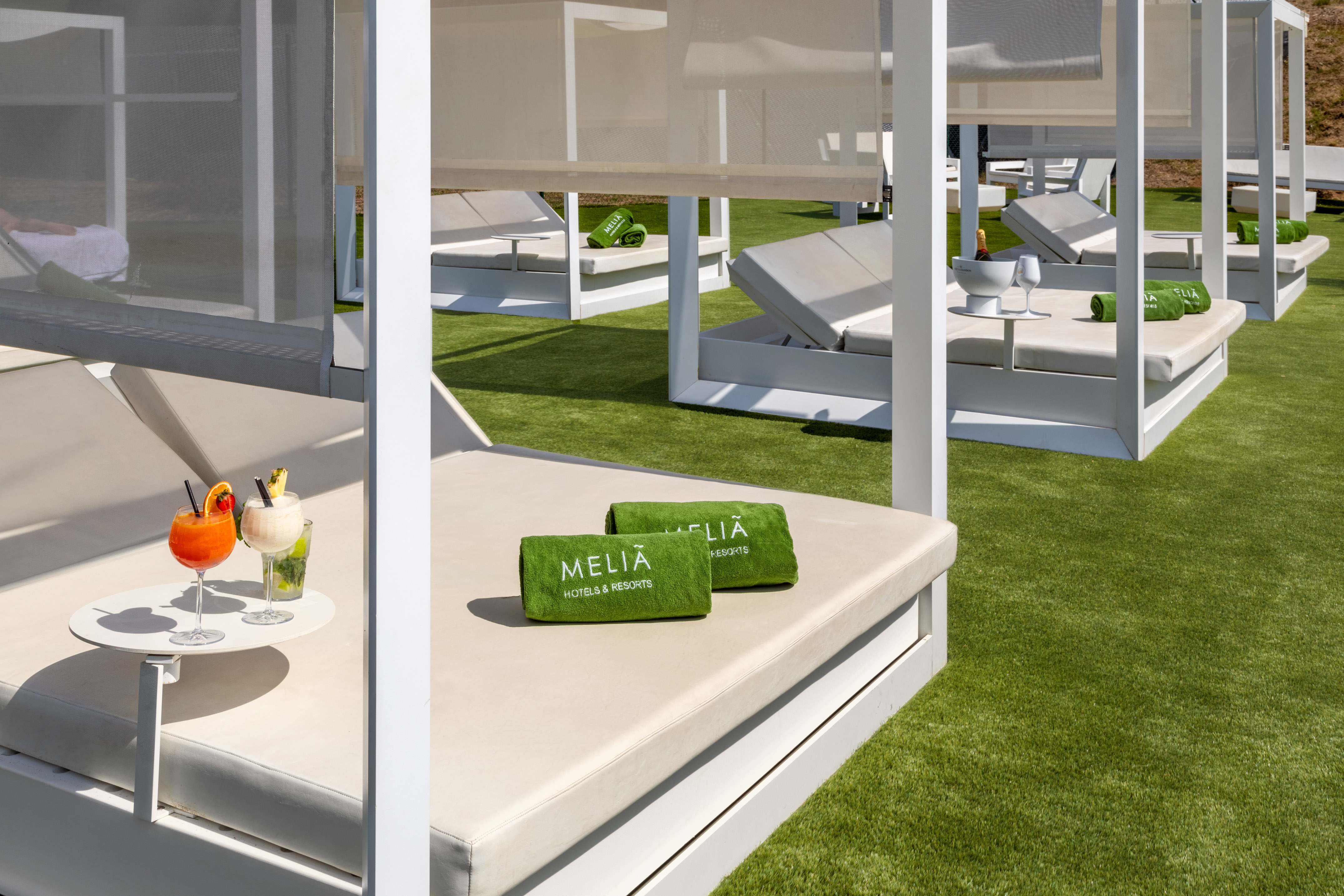 Meliá resort cabanas on green turf with cocktails and branded towels.