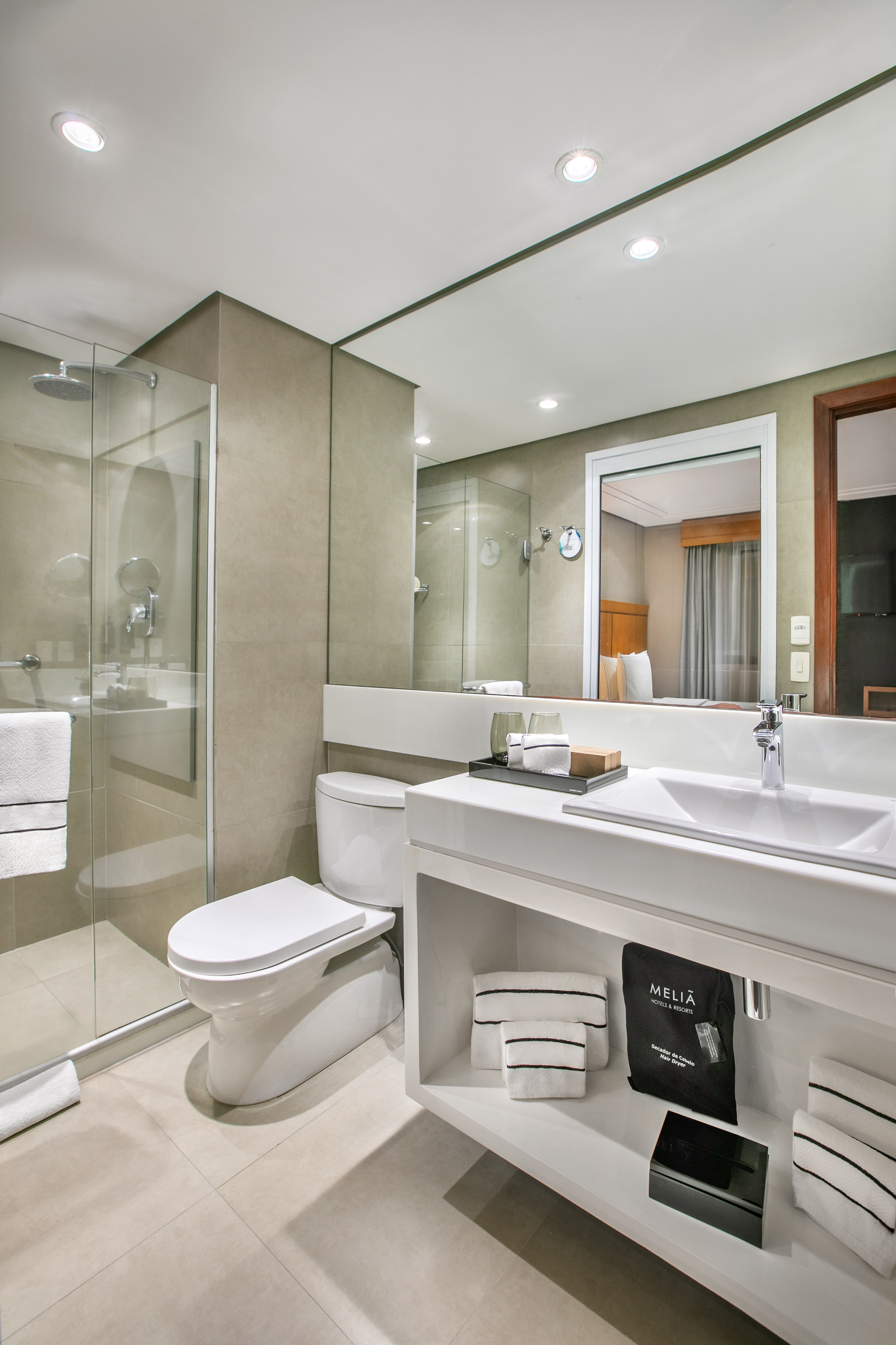 Melia hotel bathroom with modern walk-in shower, toilet, vanity sink and mirror.