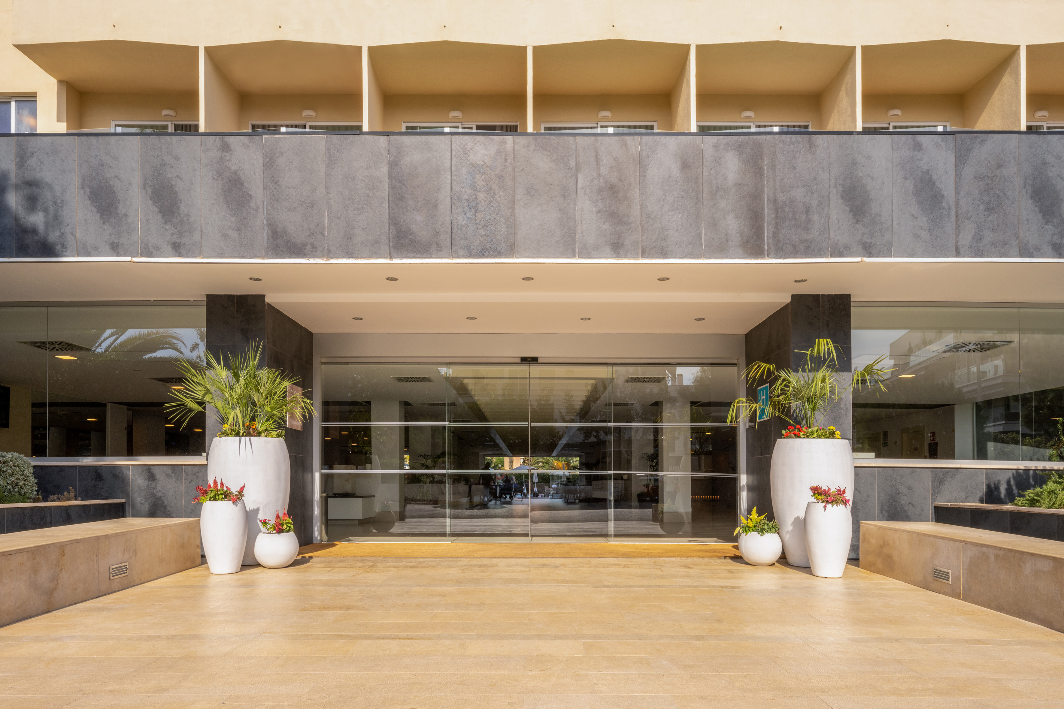 Hotel resort entrance, automatic glass doors, potted palms & red flowers.