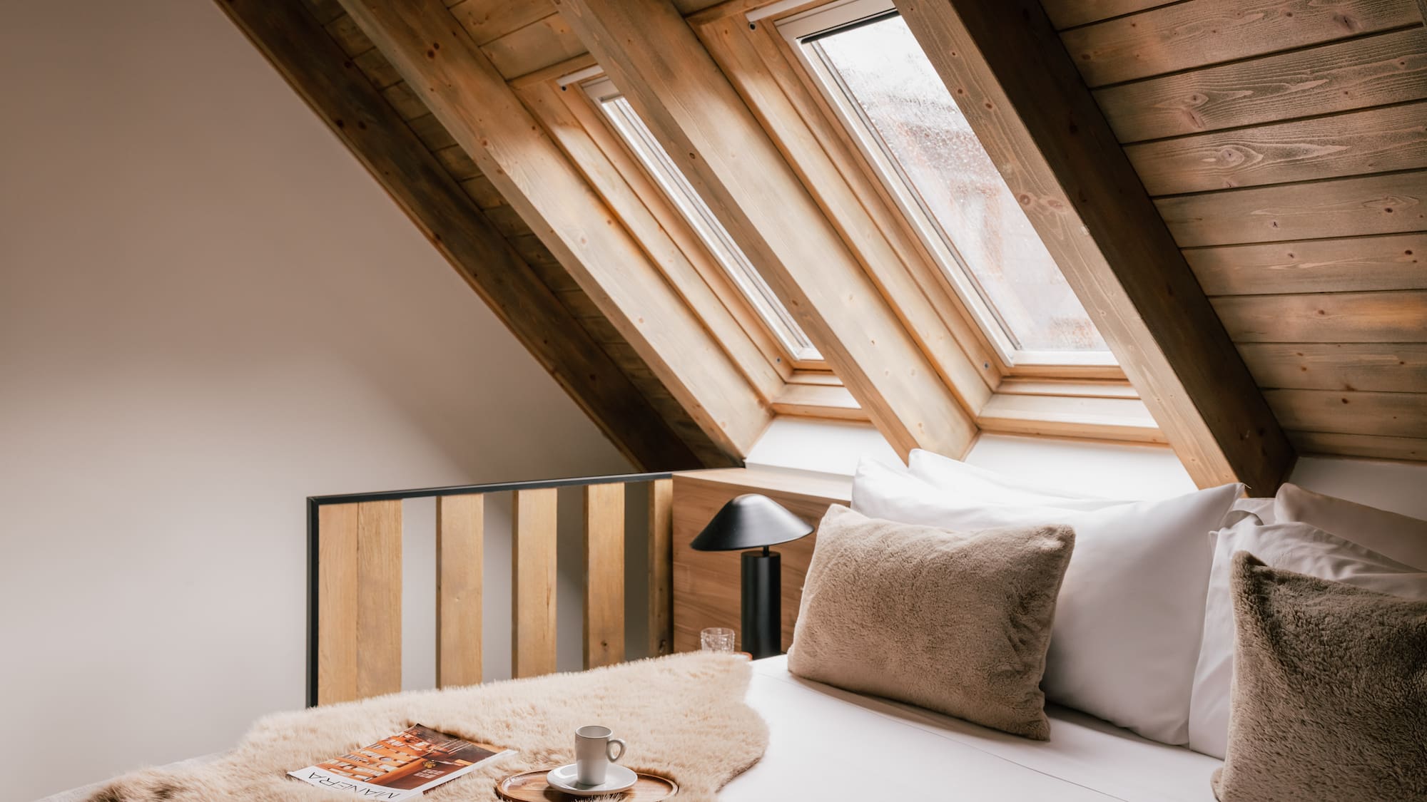 Cozy attic bedroom with wooden ceiling, skylights, and comfortable bed.