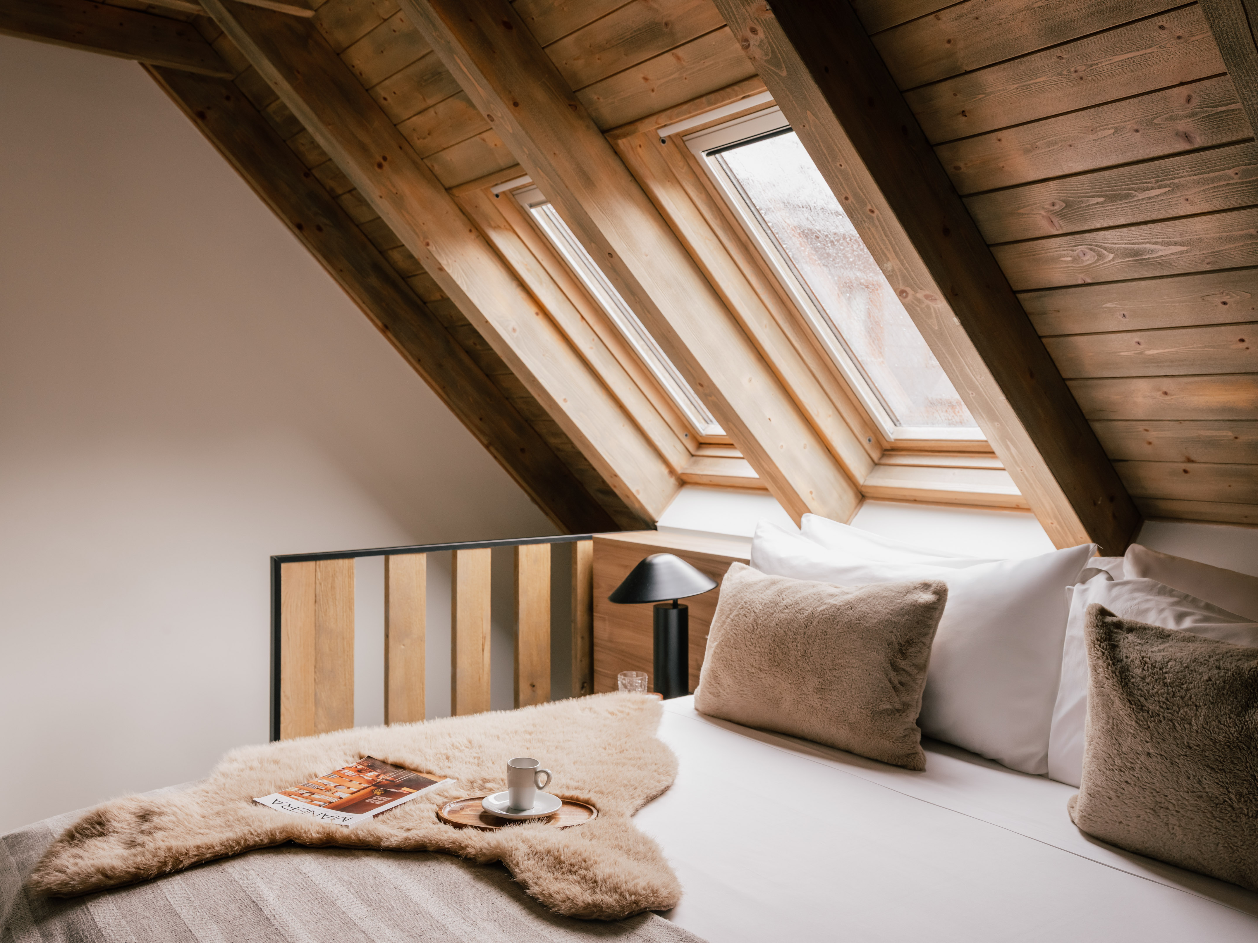 Cozy attic bedroom with wooden ceiling, skylights, and comfortable bed.
