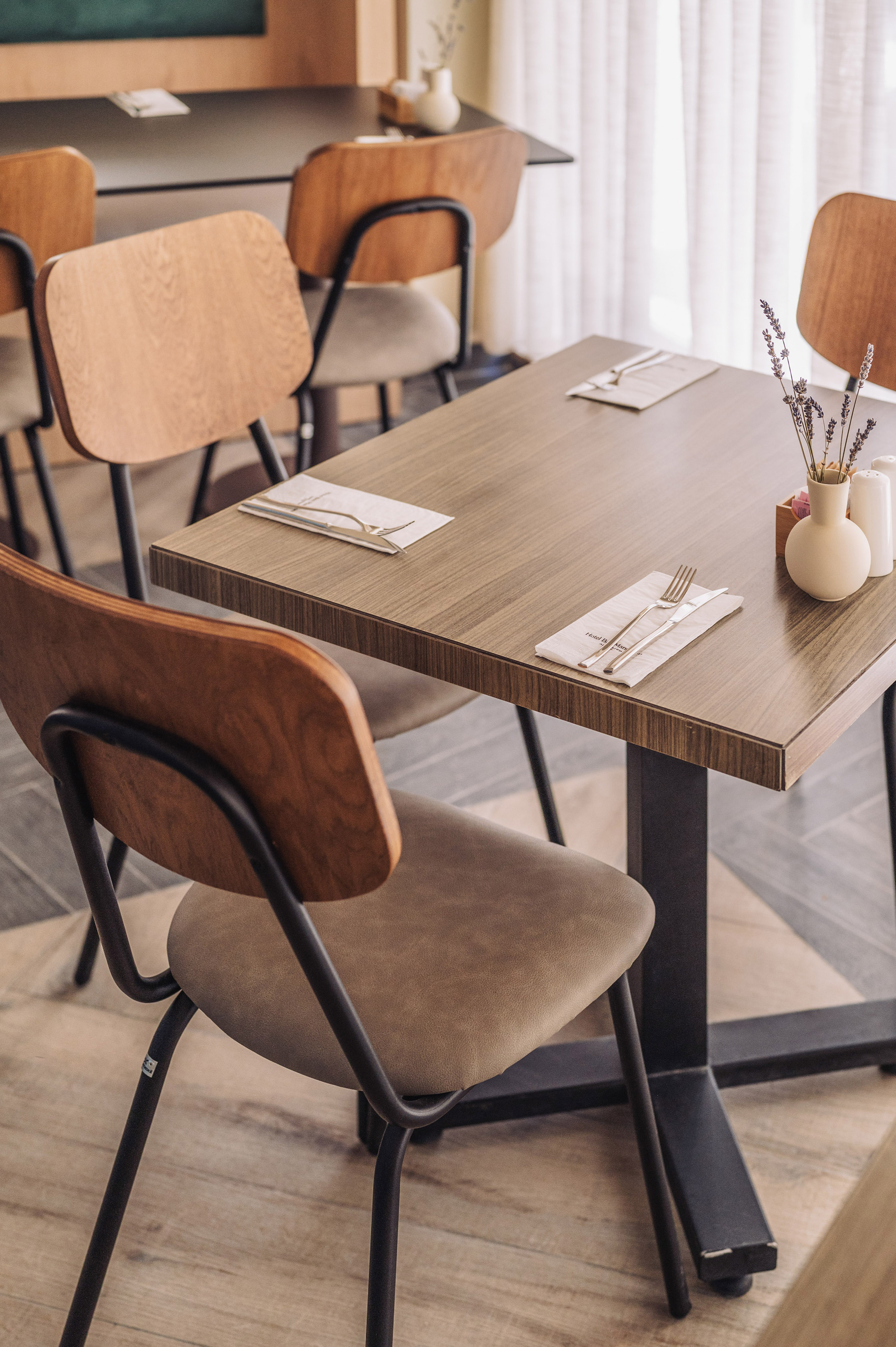 Modern restaurant dining table set with cutlery, lavender vase, and wooden chairs.
