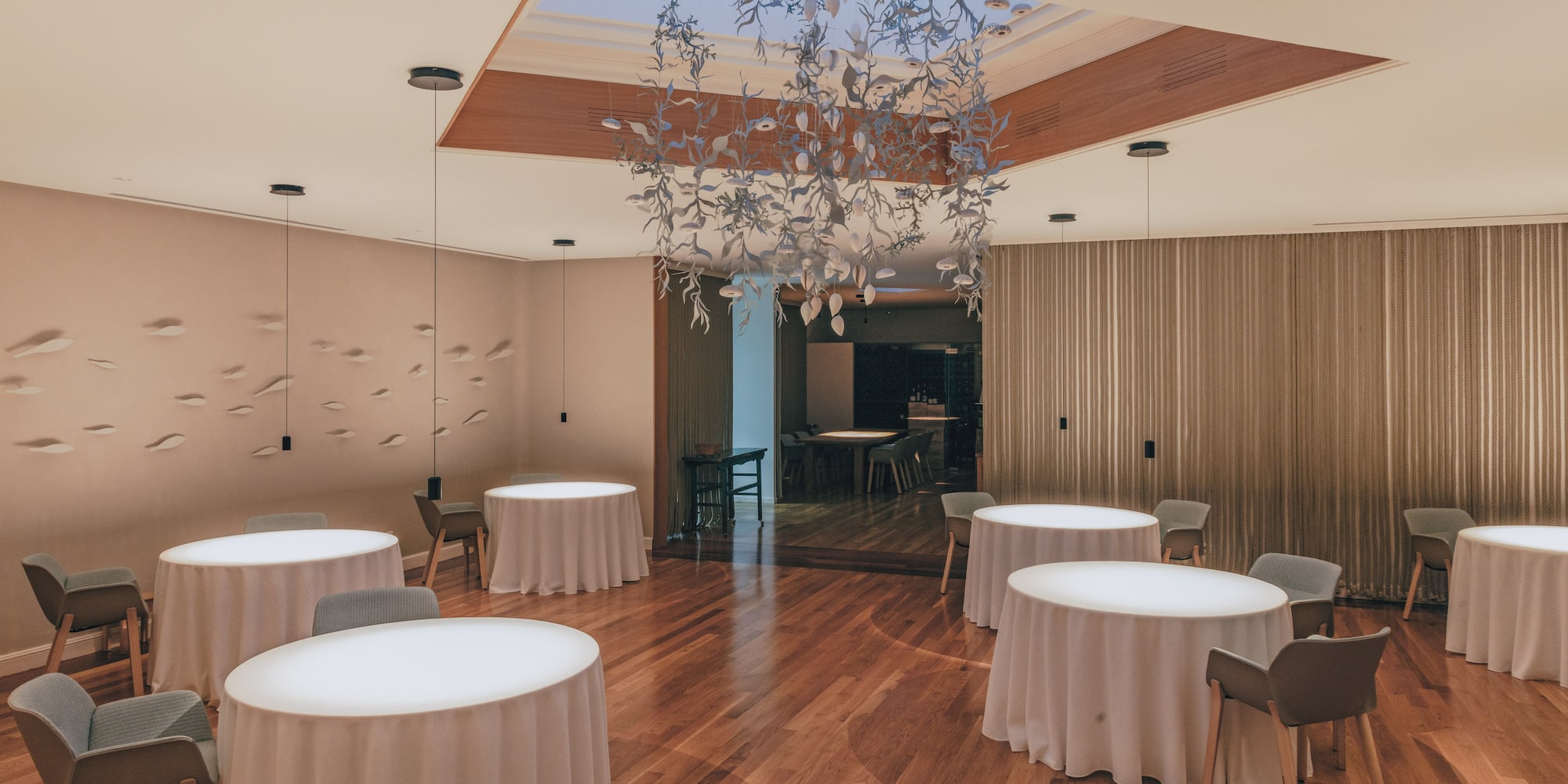 Modern fine dining restaurant with minimalist tables, wood floor, and art chandelier.